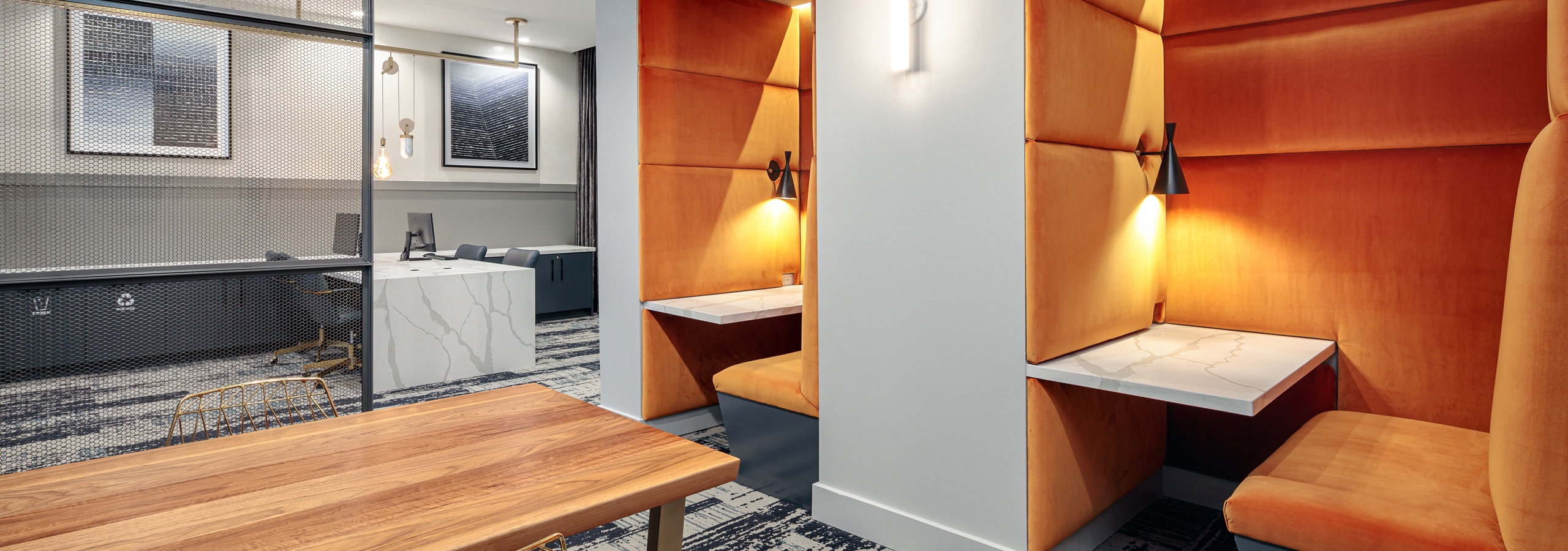 Co working space at AMLI Addison with a long wooden table and two orange nooks with a built in desk and booth seating