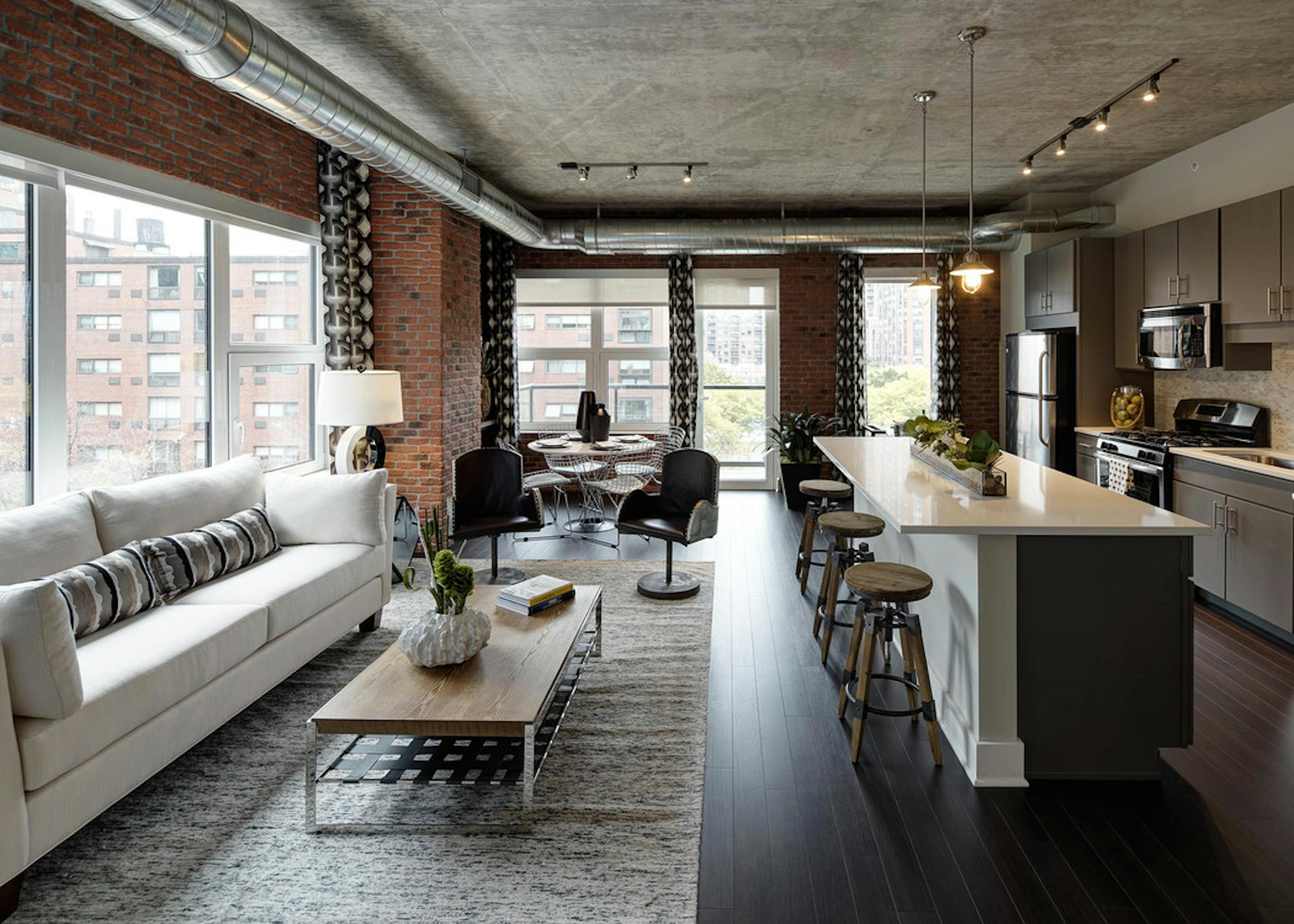 Interior view of living room and kitchen at AMLI Lofts featuring exposed brick wall with dark flooring and quartz countertops