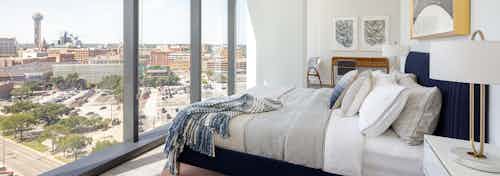Interior view of AMLI Fountain Place apartment bedroom with navy blue bed facing large wall of windows and view of Dallas