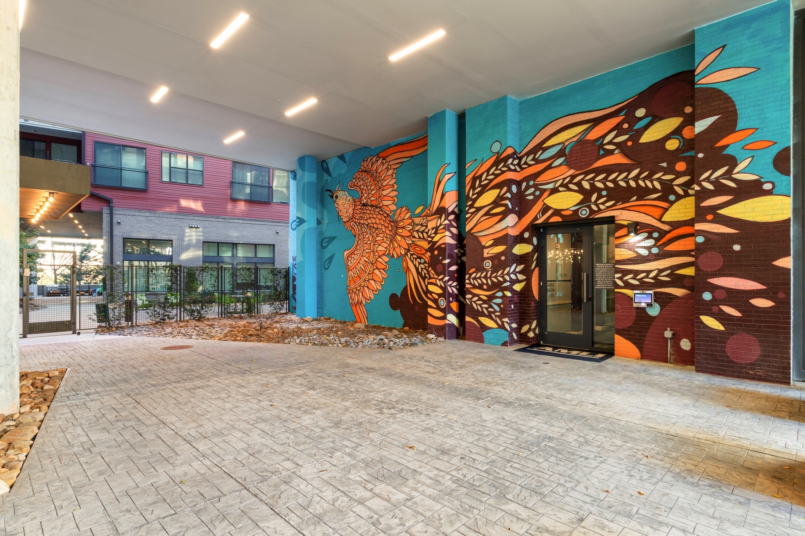Side view of AMLI Westside apartments leasing office entrance with colorful bright mural of flying bird on blue brick wall