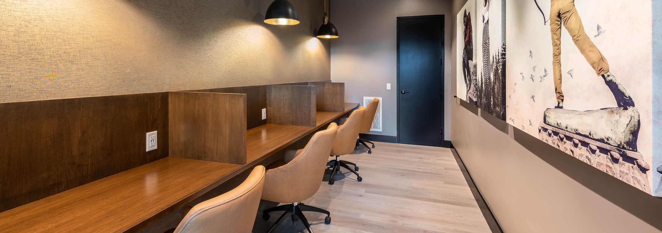 AMLI Art District workspace with partitioned desks and leather chairs with overhead lights and canvas paintings on the wall