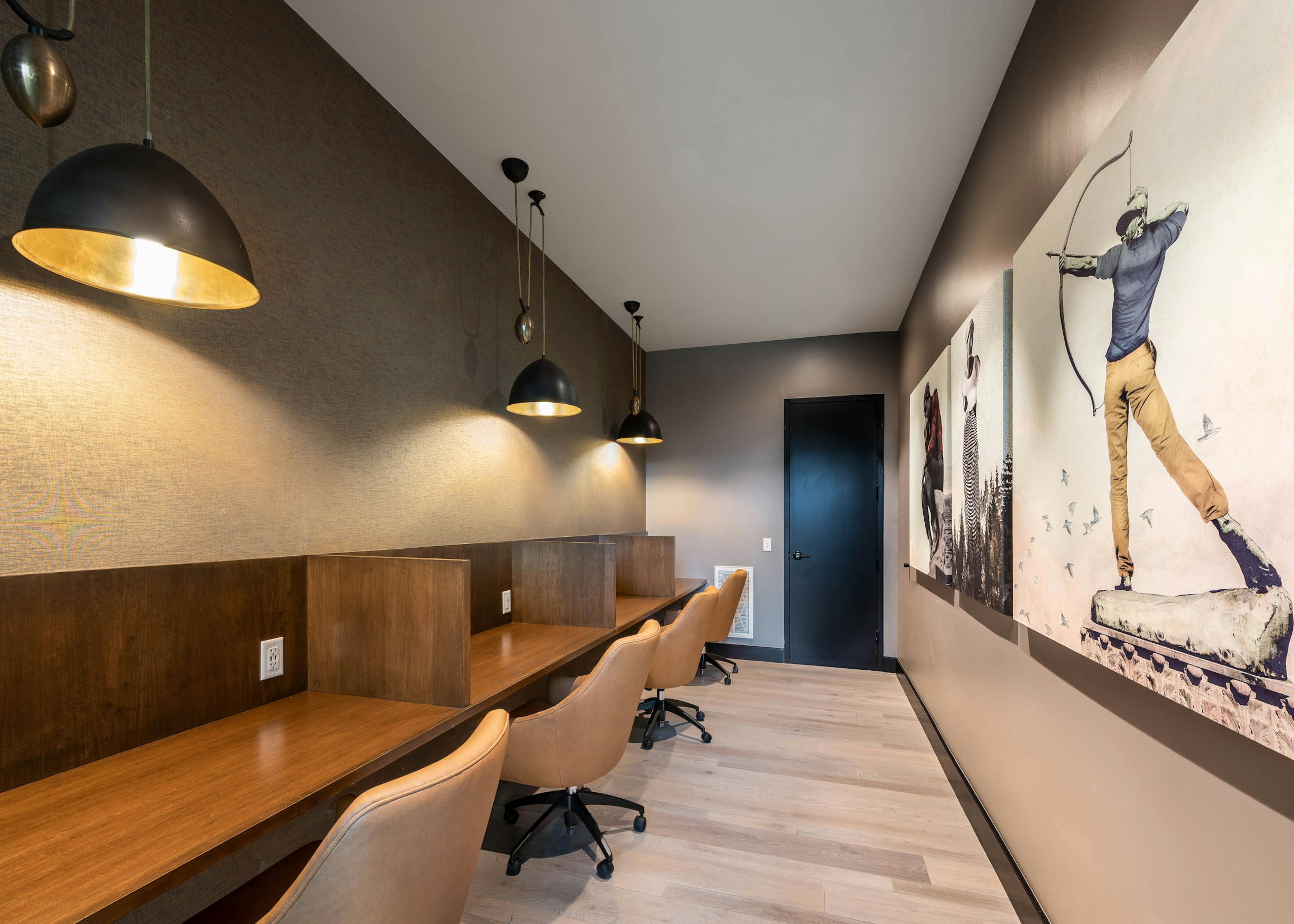 AMLI Art District workspace with partitioned desks and leather chairs with overhead lights and canvas paintings on the wall