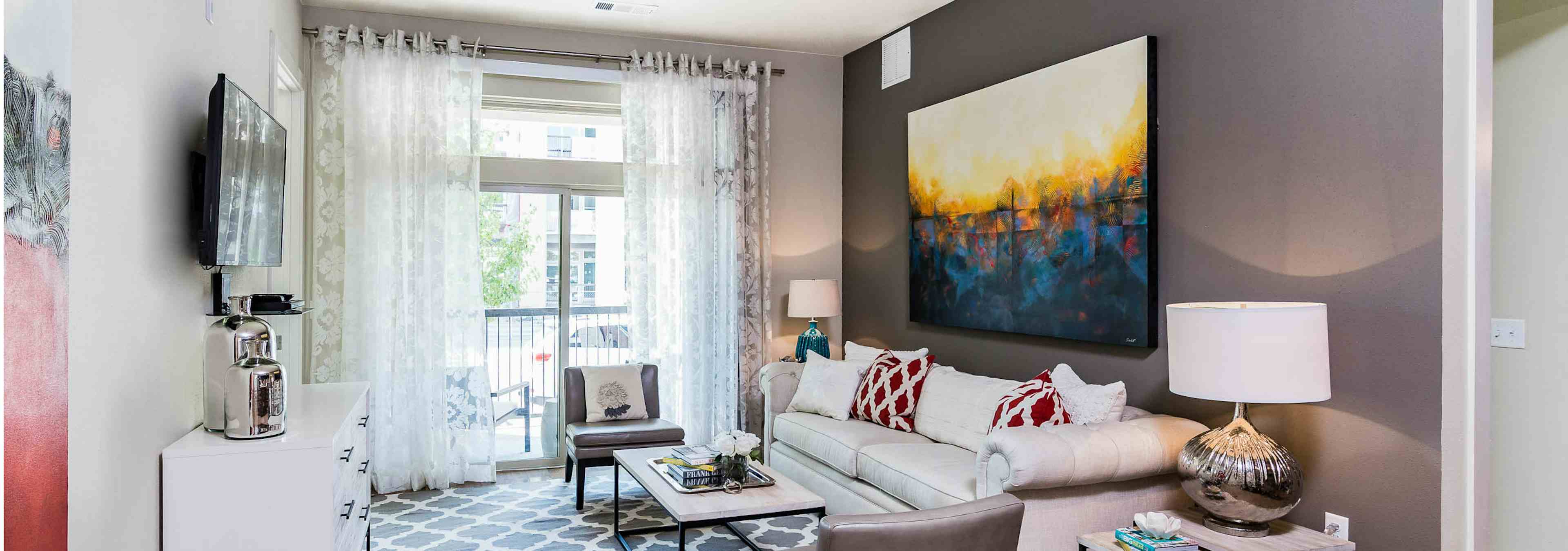 Interior view of AMLI RidgeGate living room with sofa, centered wall art facing windows with sheer curtains to private patio