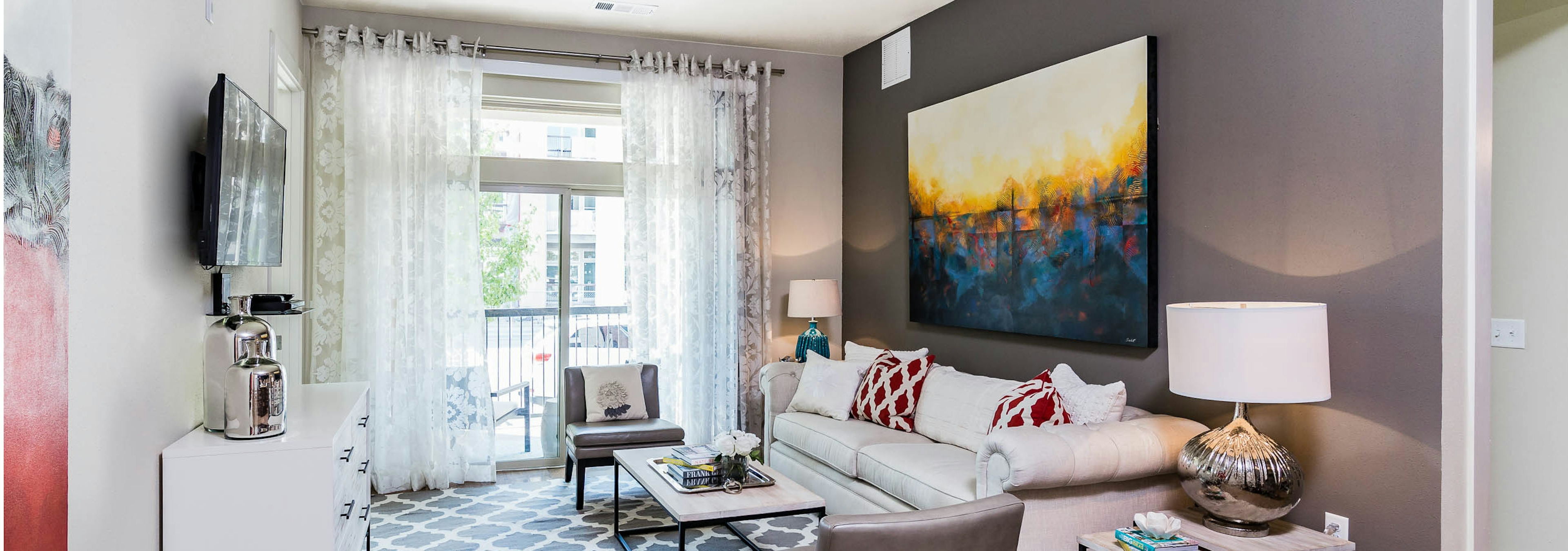 Interior view of AMLI RidgeGate living room with sofa, centered wall art facing windows with sheer curtains to private patio