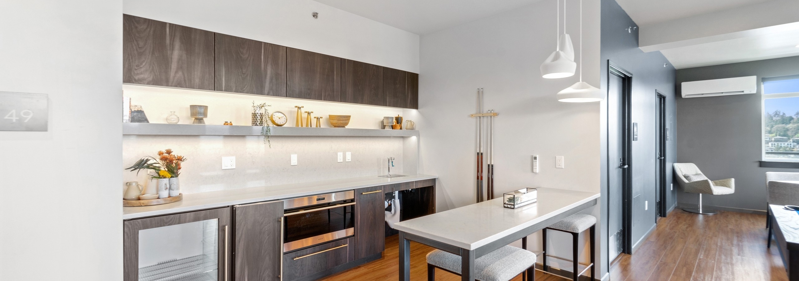 Bellevue Park sky lounge with serving kitchen with brown cabinets and white table with 2 stools and white pendant lights overhead