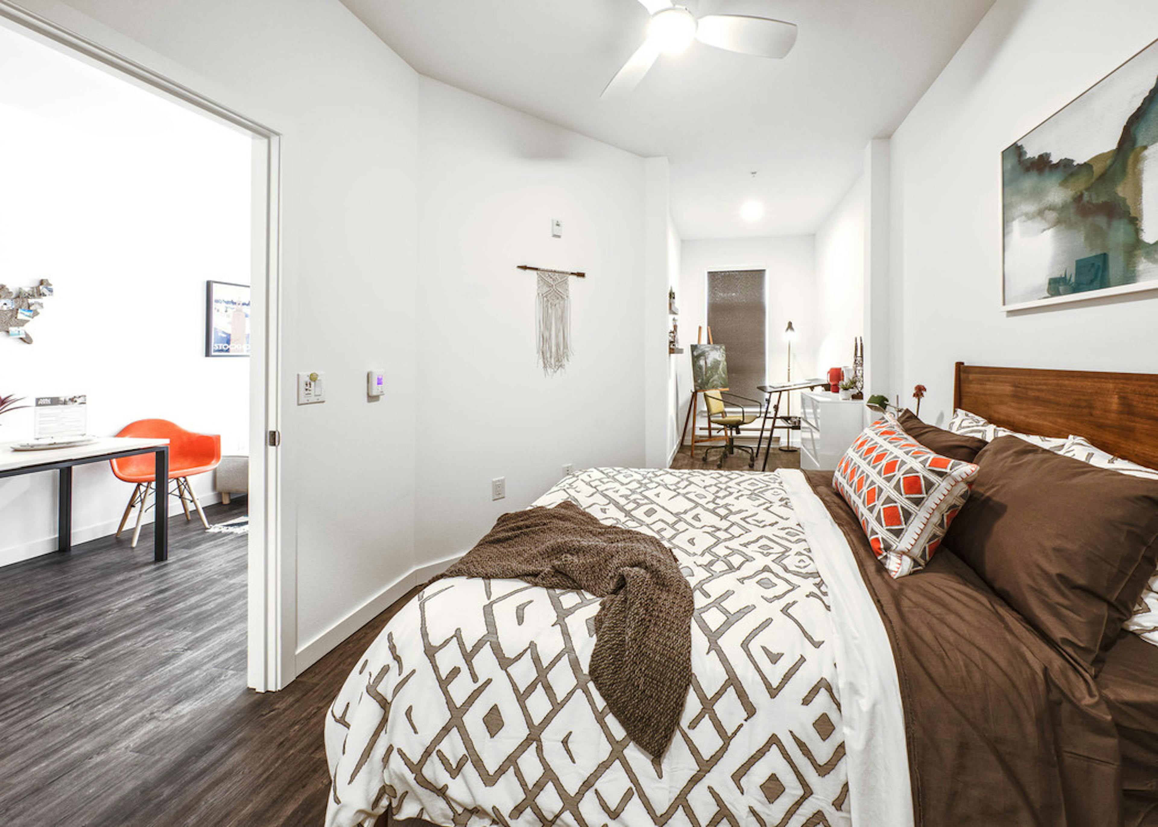 View of a bedroom of a AMLI Wallingford apartment with queen size bed large window and slight view of the kitchen living room 