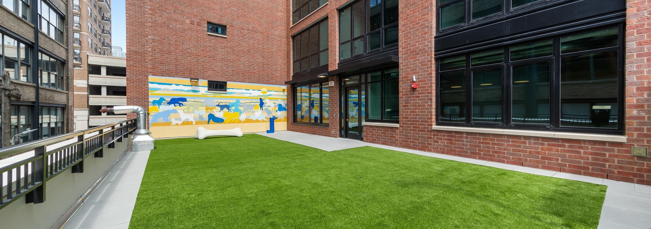 Daytime view of spacious outdoor pet park at AMLI 808 with green turf surrounded by the community’s brick exterior
