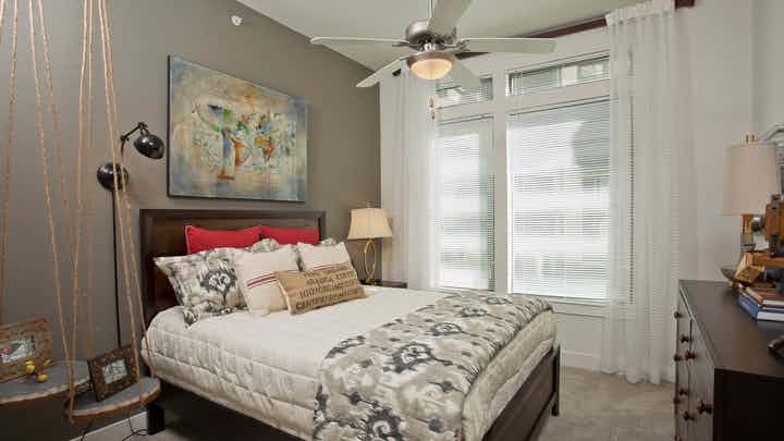 Bedroom at AMLI 5350 with a white bed against a dark grey accent wall next to a large window with sunny daytime views