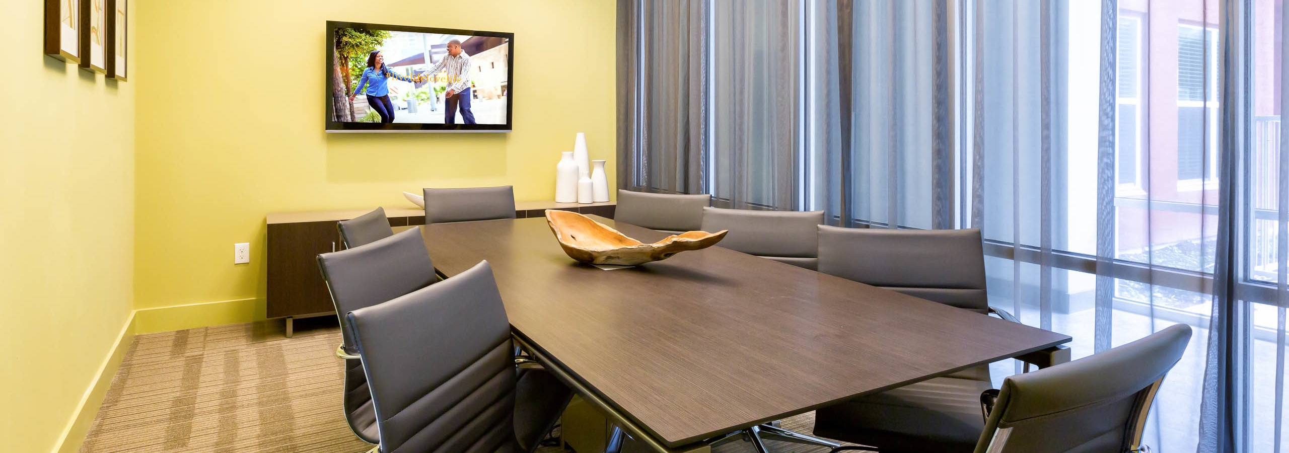 AMLI at Mueller conference room with yellow walls and light flooring with a long desk and office chairs near tall windows