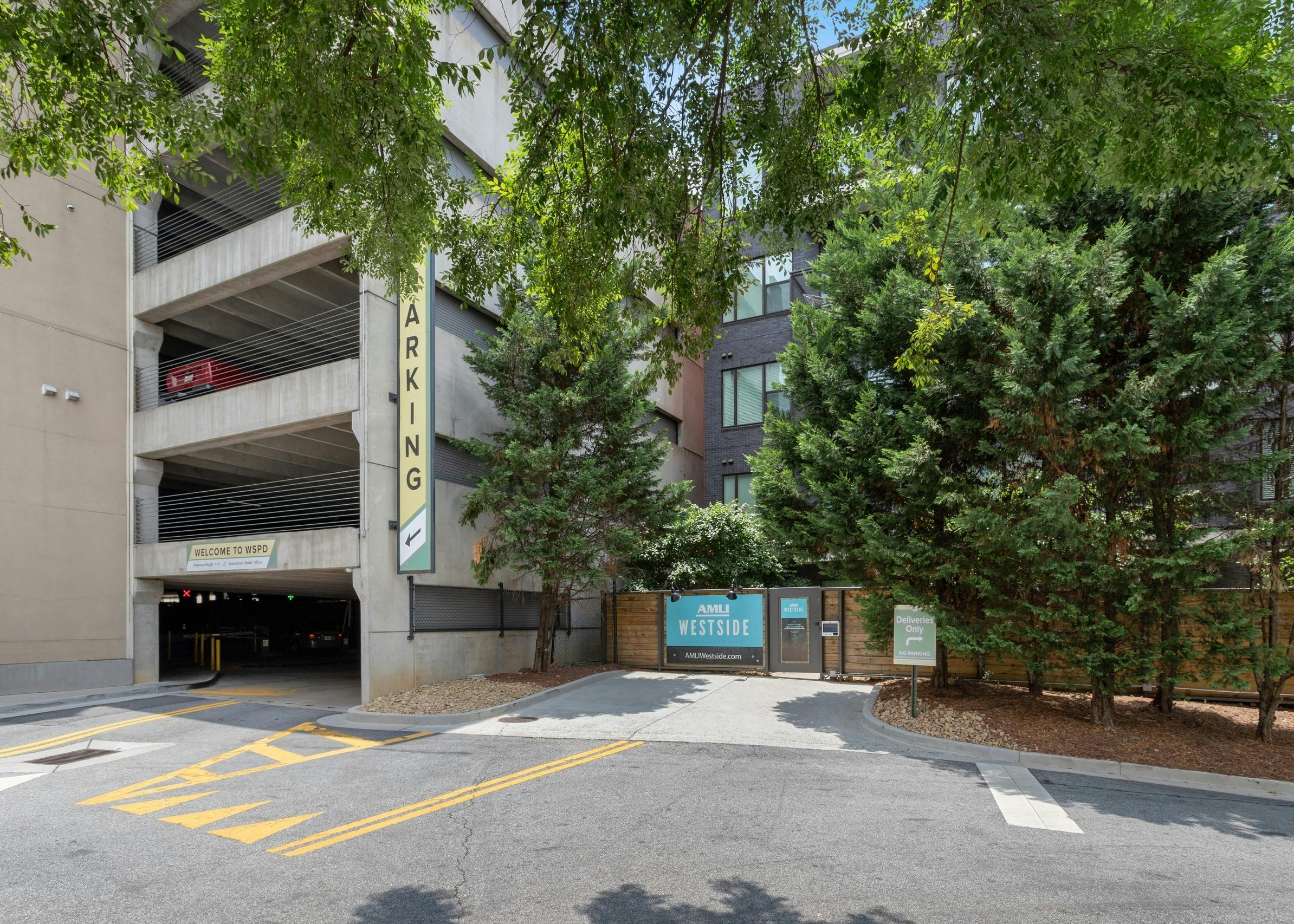 Daytime view of parking structure entrance and pedestrian gate with call box surrounded by many lush trees at AMLI Westside