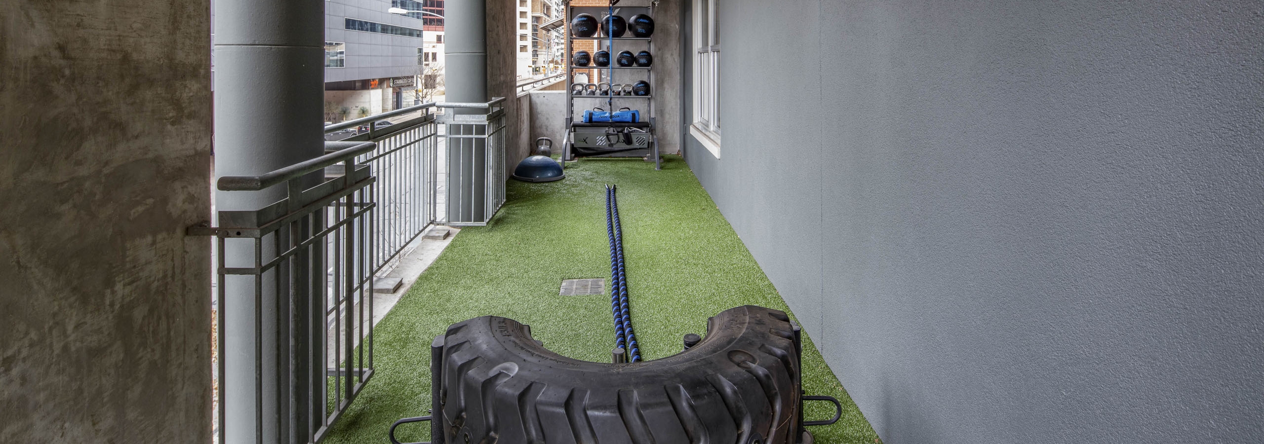 AMLI Downtown outdoor fitness area with a tire flipping machine and free weights on green turf and with downtown Austin views