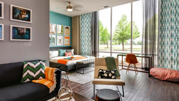 Bedroom at AMLI at Mueller with large floor to ceiling windows and dark wood floors with orange and blue decor accents