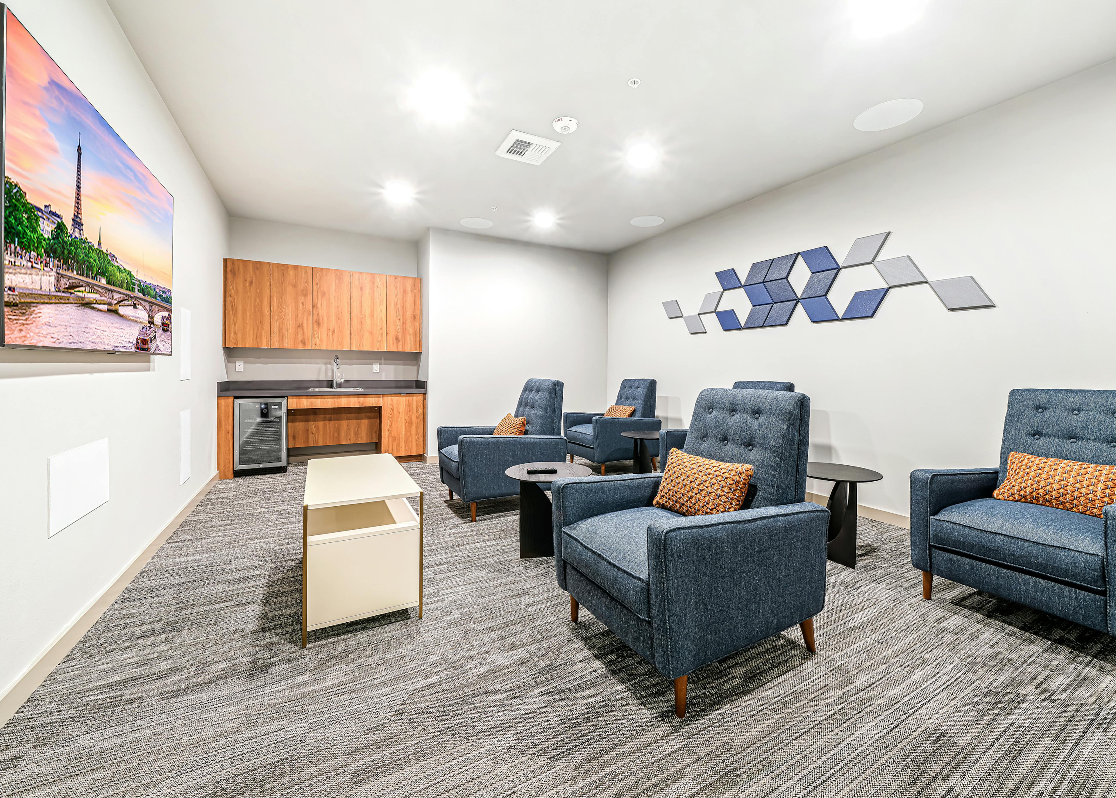 AMLI Spring District theater room with large mounted TV and 6 blue chairs and wood cabinets with refrigerator and sink