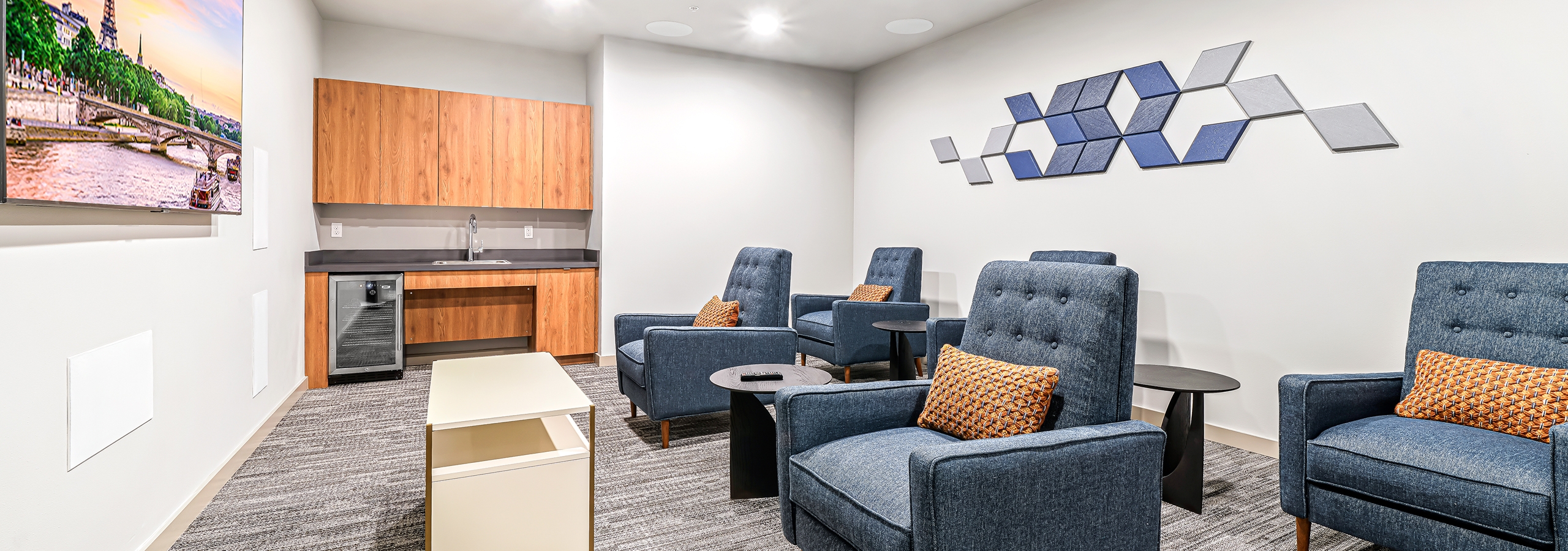 AMLI Spring District theater room with large mounted TV and 6 blue chairs and wood cabinets with refrigerator and sink