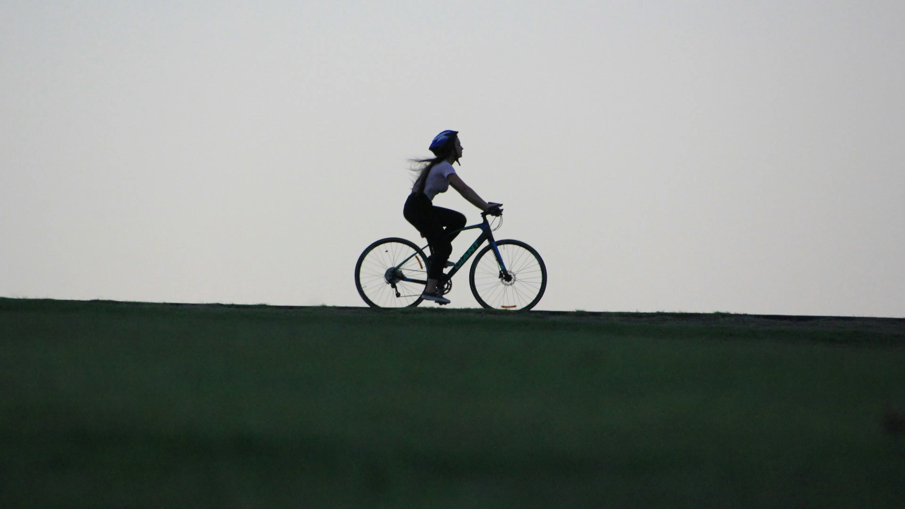 A woman on a bike in silhouette on a hill