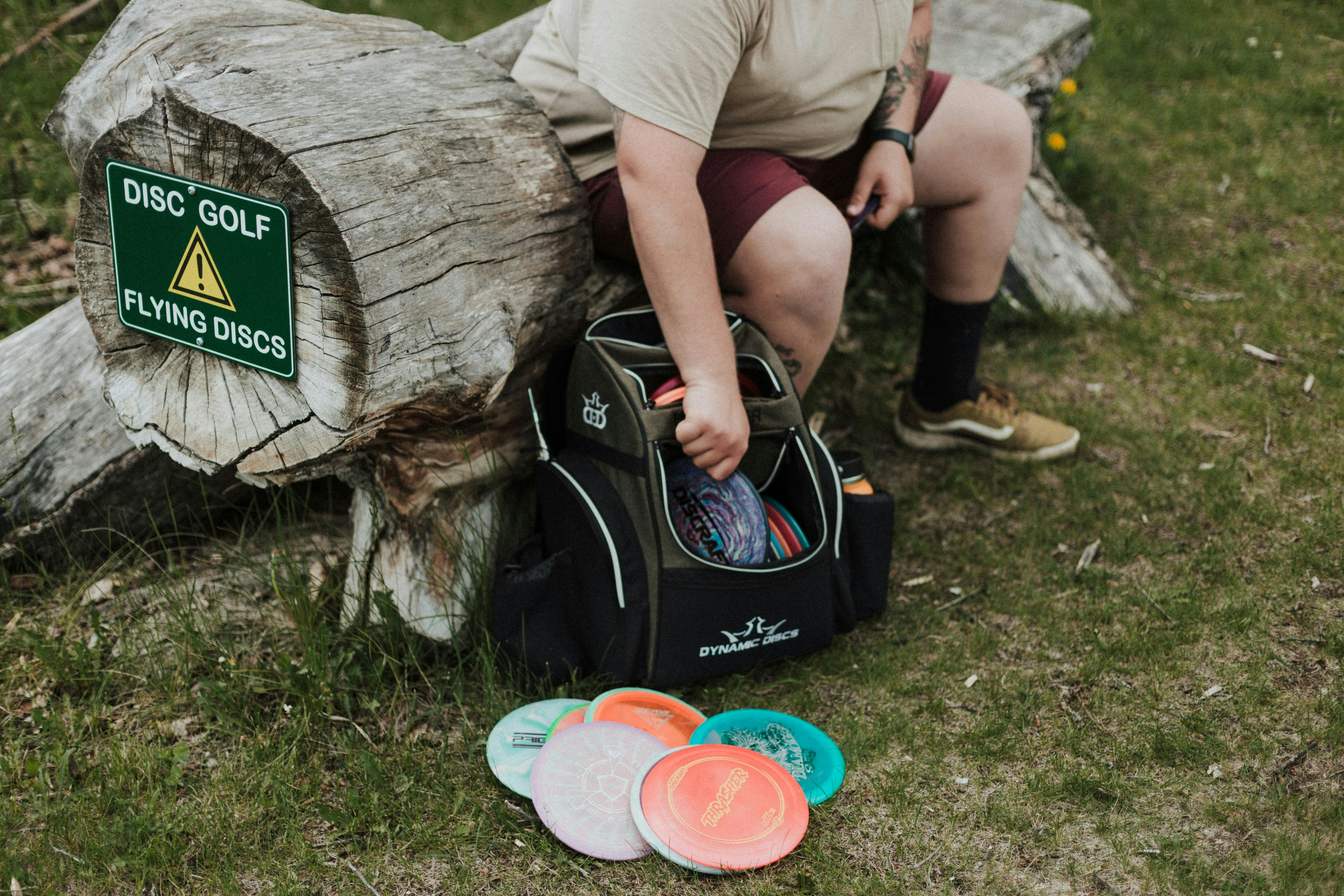 A disc golfer reaching into a bag of discs while sat on a log