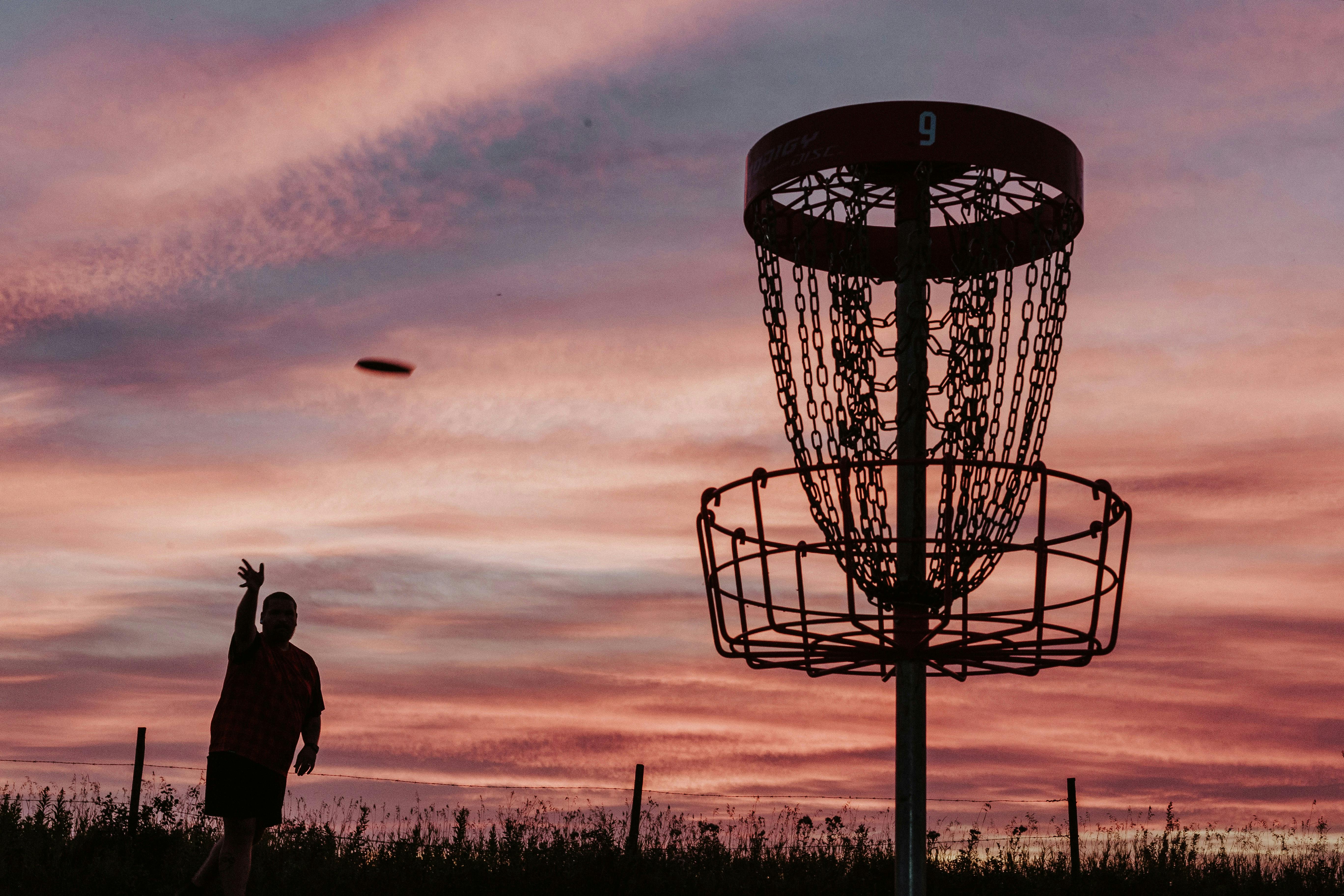 A silhouette of a disc golfer throwing a putt into a net