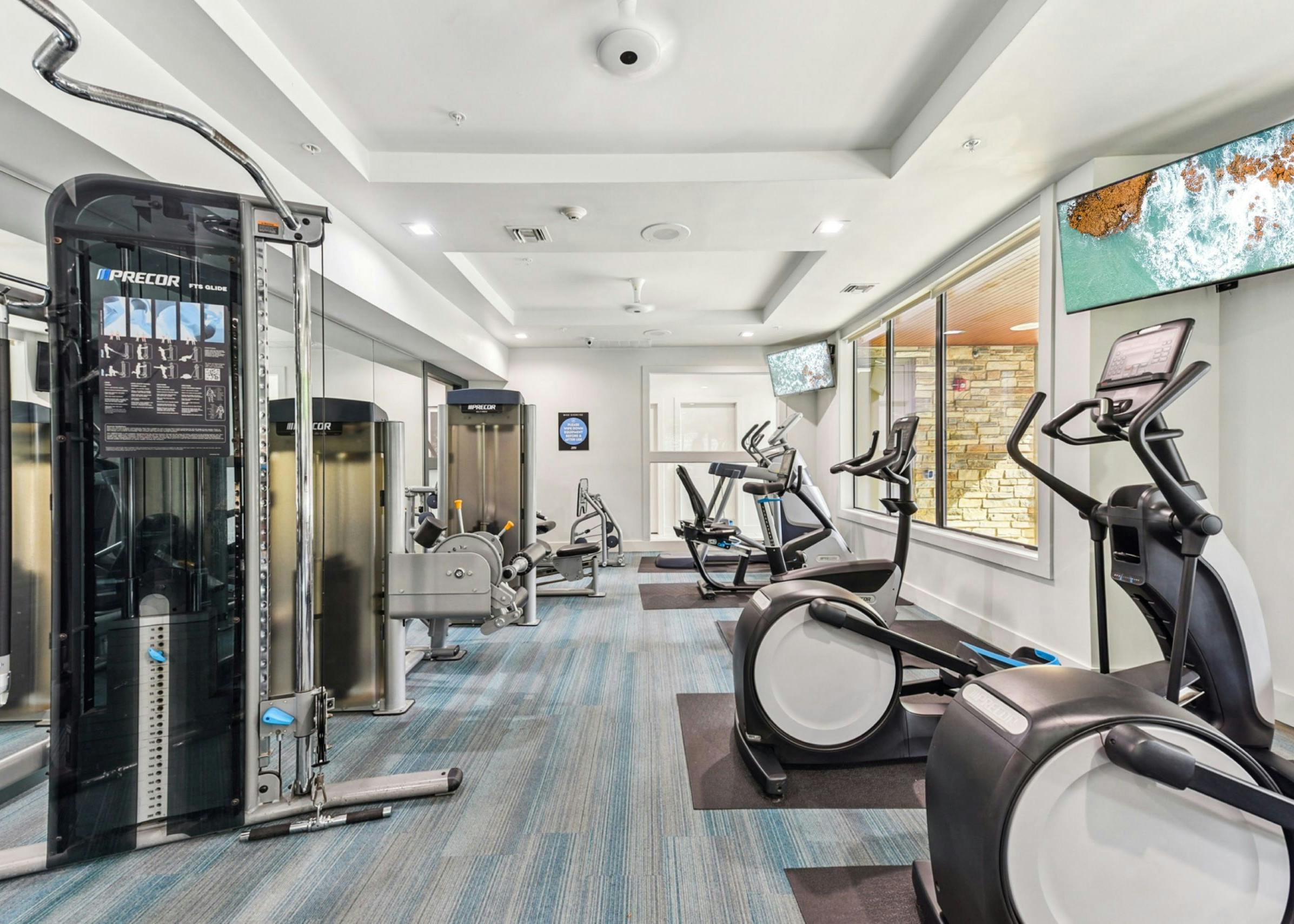 Modern fitness center at AMLI Covered Bridge apartments with various exercise equipment, large windows and flat-screen TVs