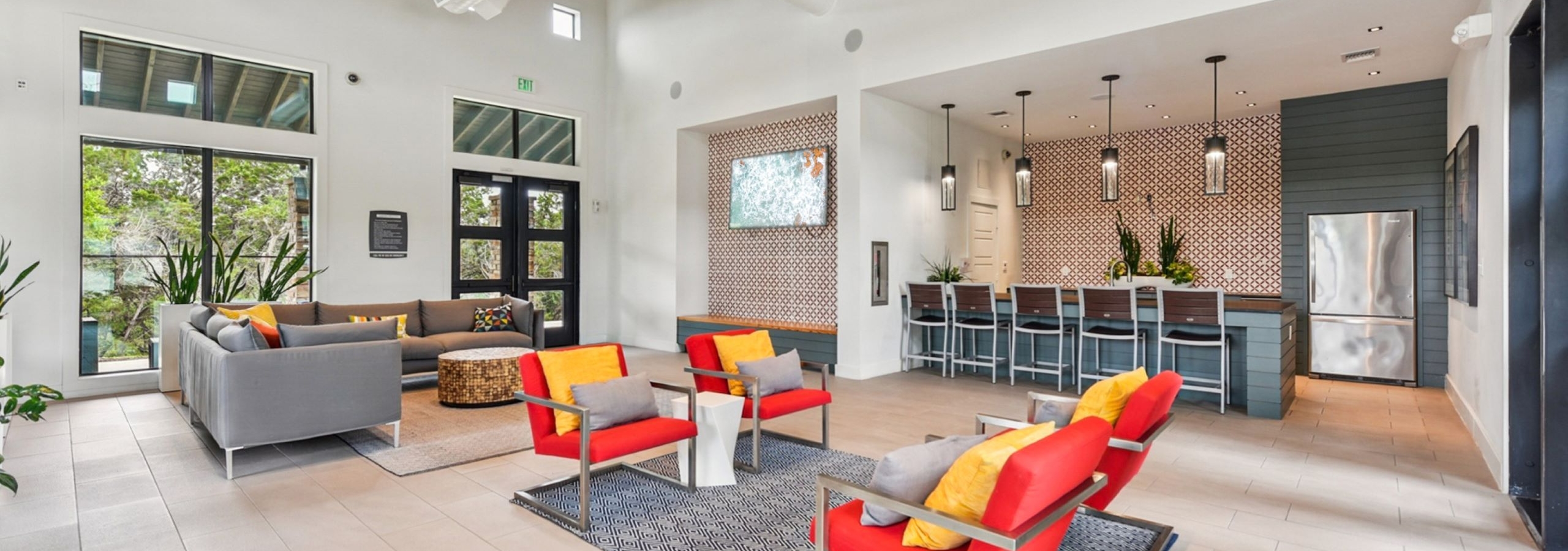 Modern clubhouse at AMLI Covered Bridge apartments with two colorful seating areas, kitchen with bar stools and large glass doors