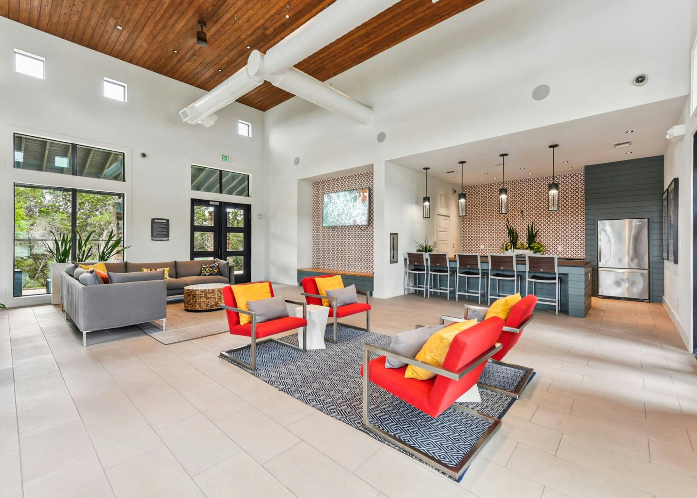 Modern clubhouse at AMLI Covered Bridge apartments with two colorful seating areas, kitchen with bar stools and large glass doors