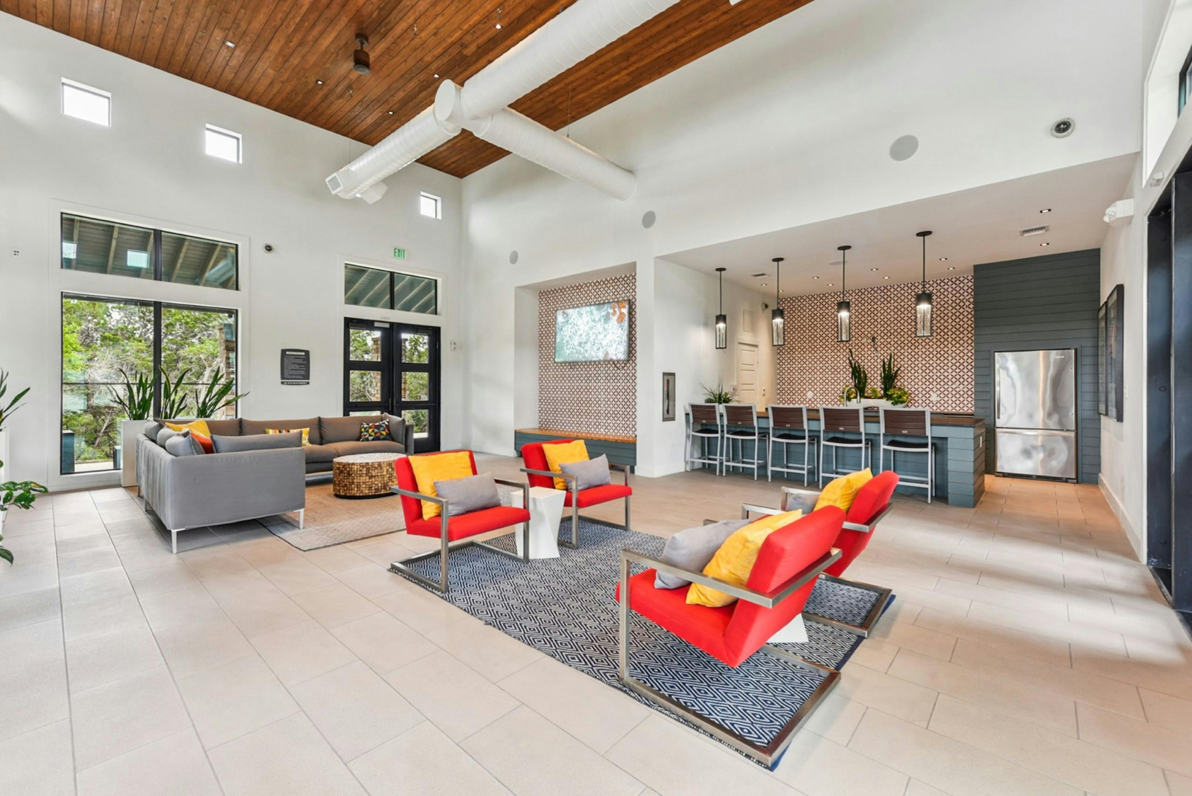 Modern clubhouse at AMLI Covered Bridge apartments with two colorful seating areas, kitchen with bar stools and large glass doors