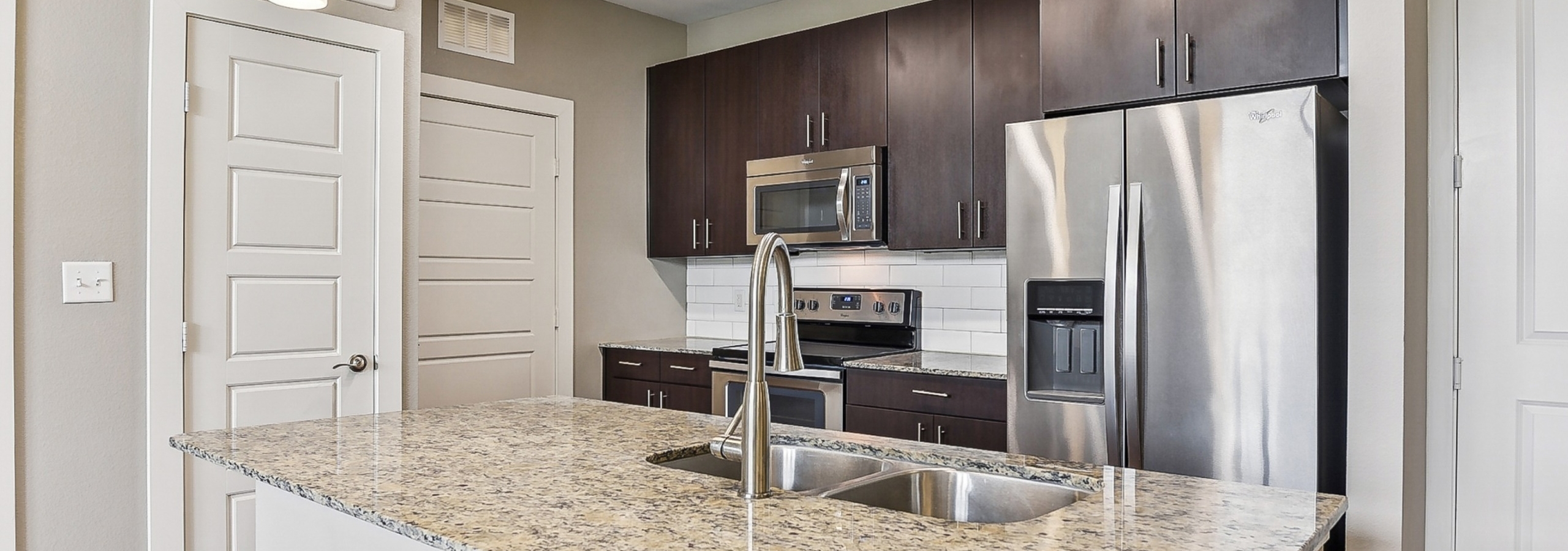 Modern kitchen at AMLI Covered Bridge apartments with granite countertop island, dark wood cabinets and stainless steel appliances