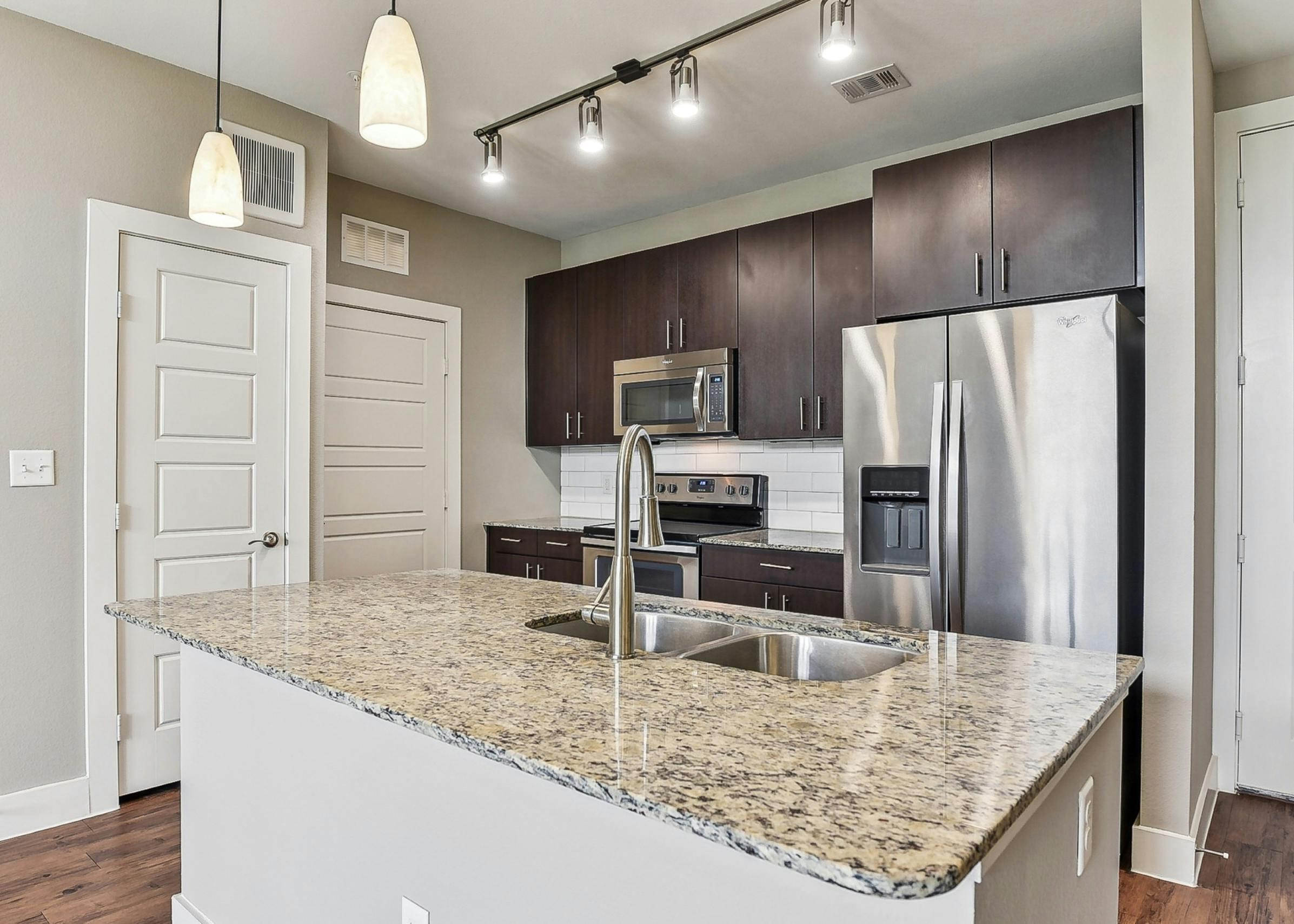 Modern kitchen at AMLI Covered Bridge apartments with granite countertop island, dark wood cabinets and stainless steel appliances