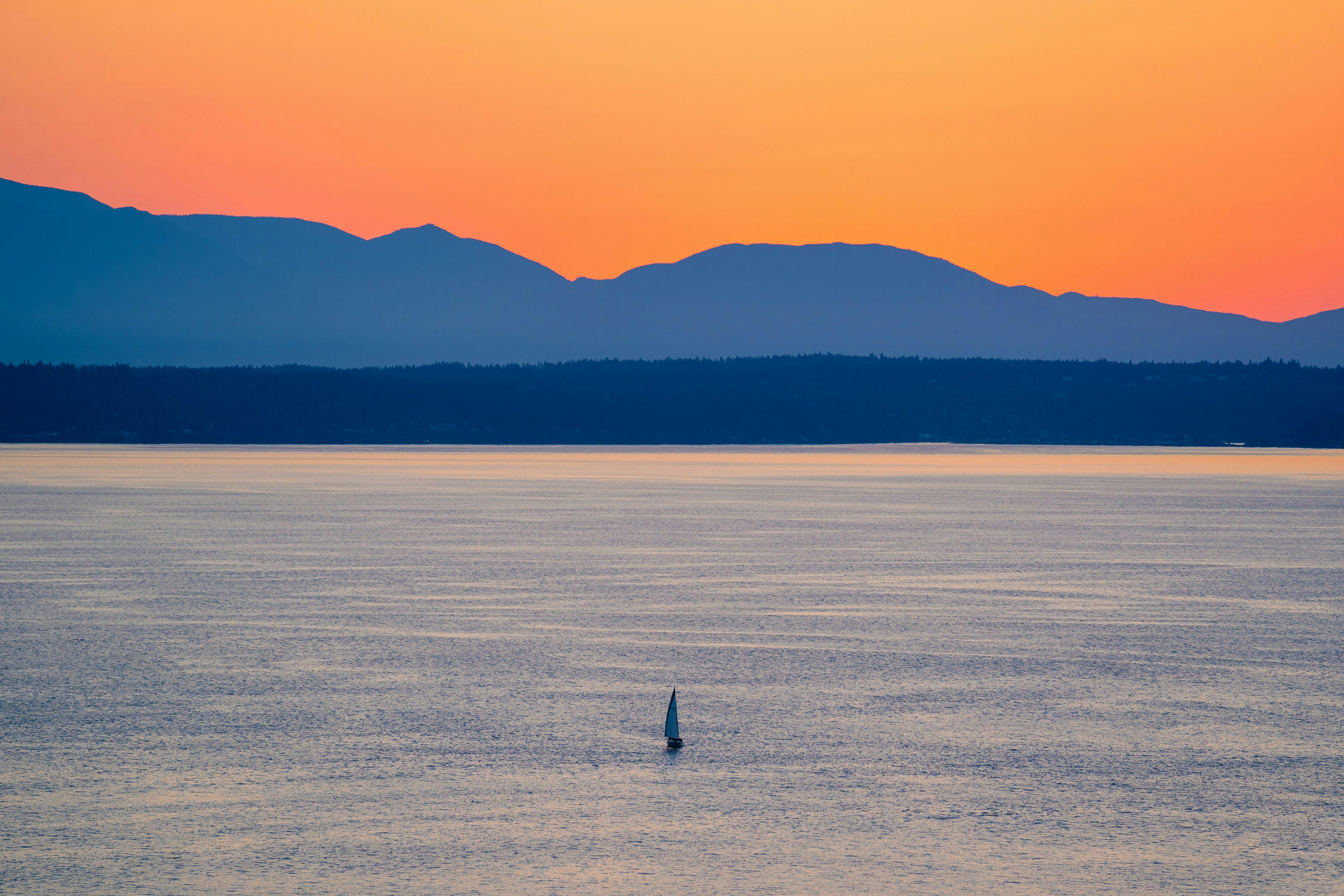 A lone sailboat in the middle of a large bay in the Puget Sound with mountains in the background
