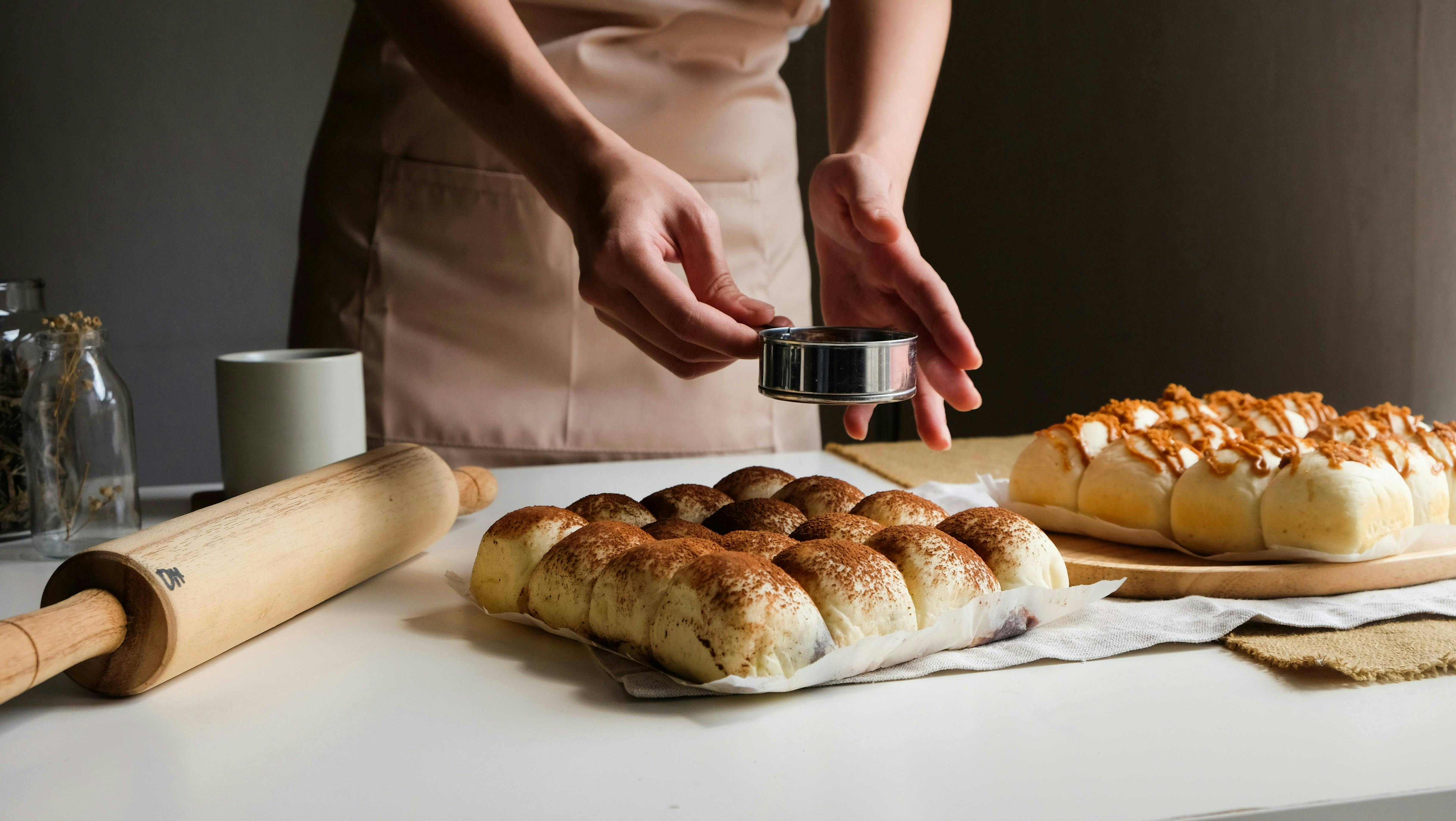 A person with an apron dusting flour over some homemade buns