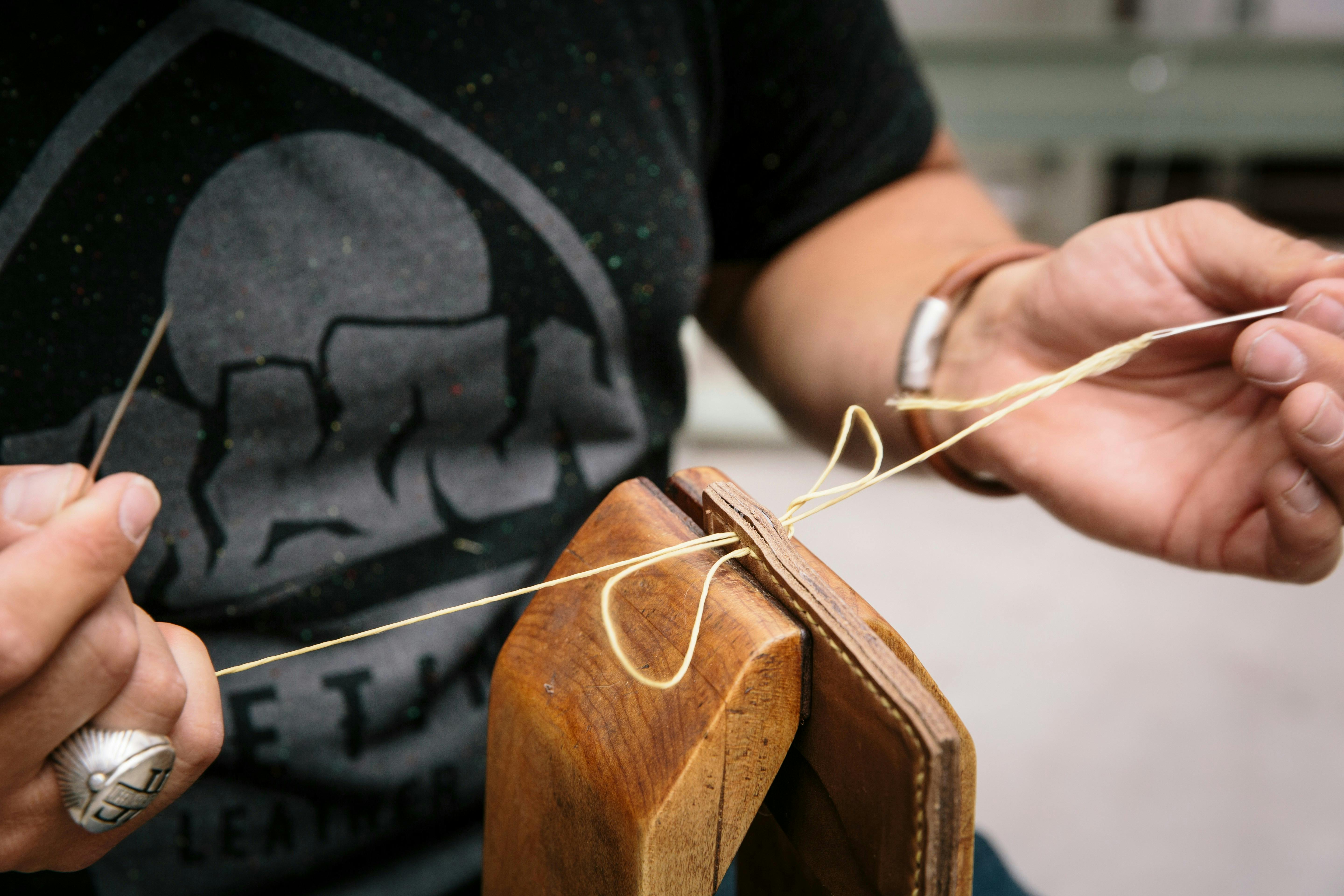 A person in a black t shirt sewing a leather wallet with sinew