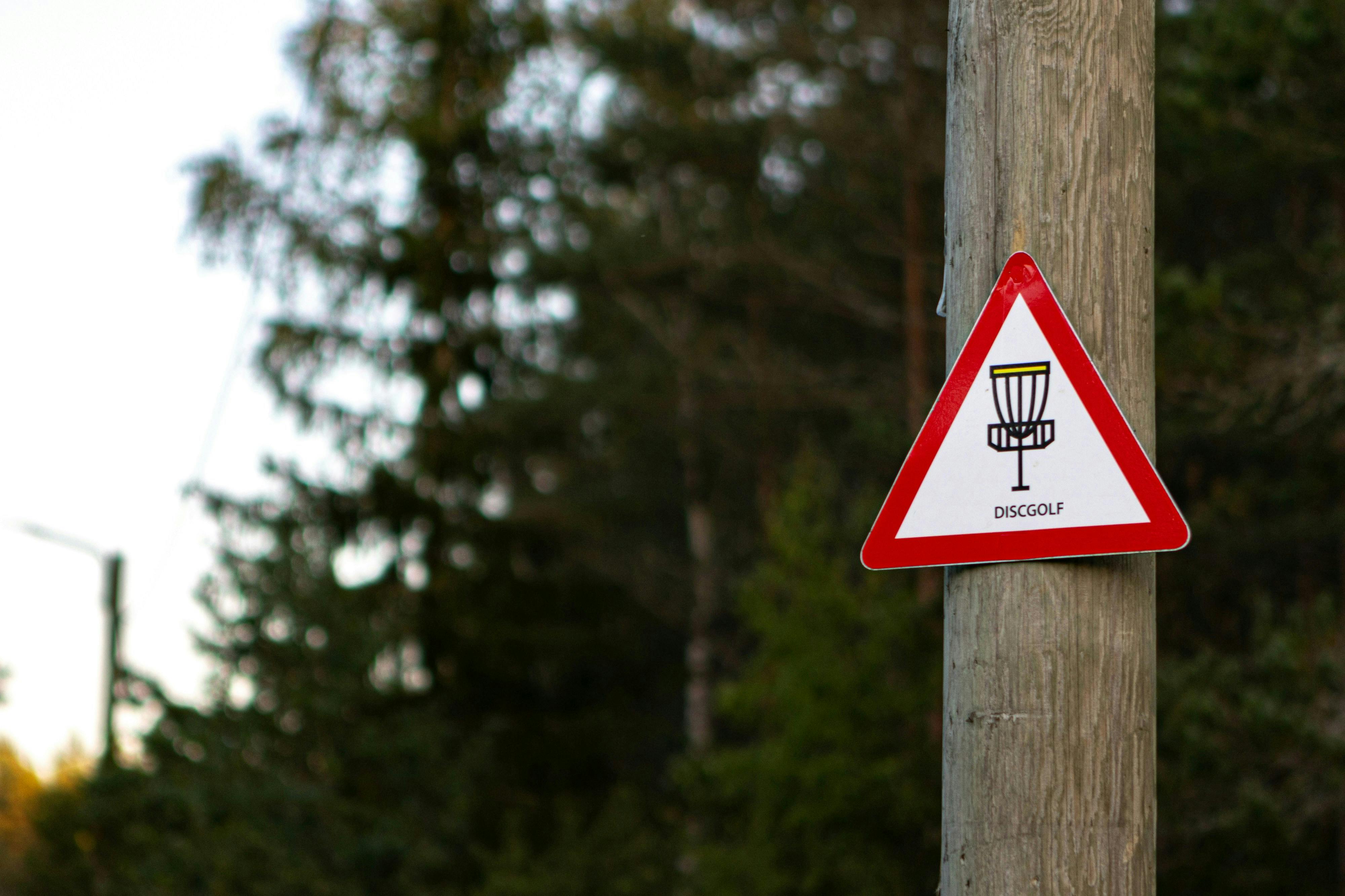A red and white triangle sign that says Disc Golf on it