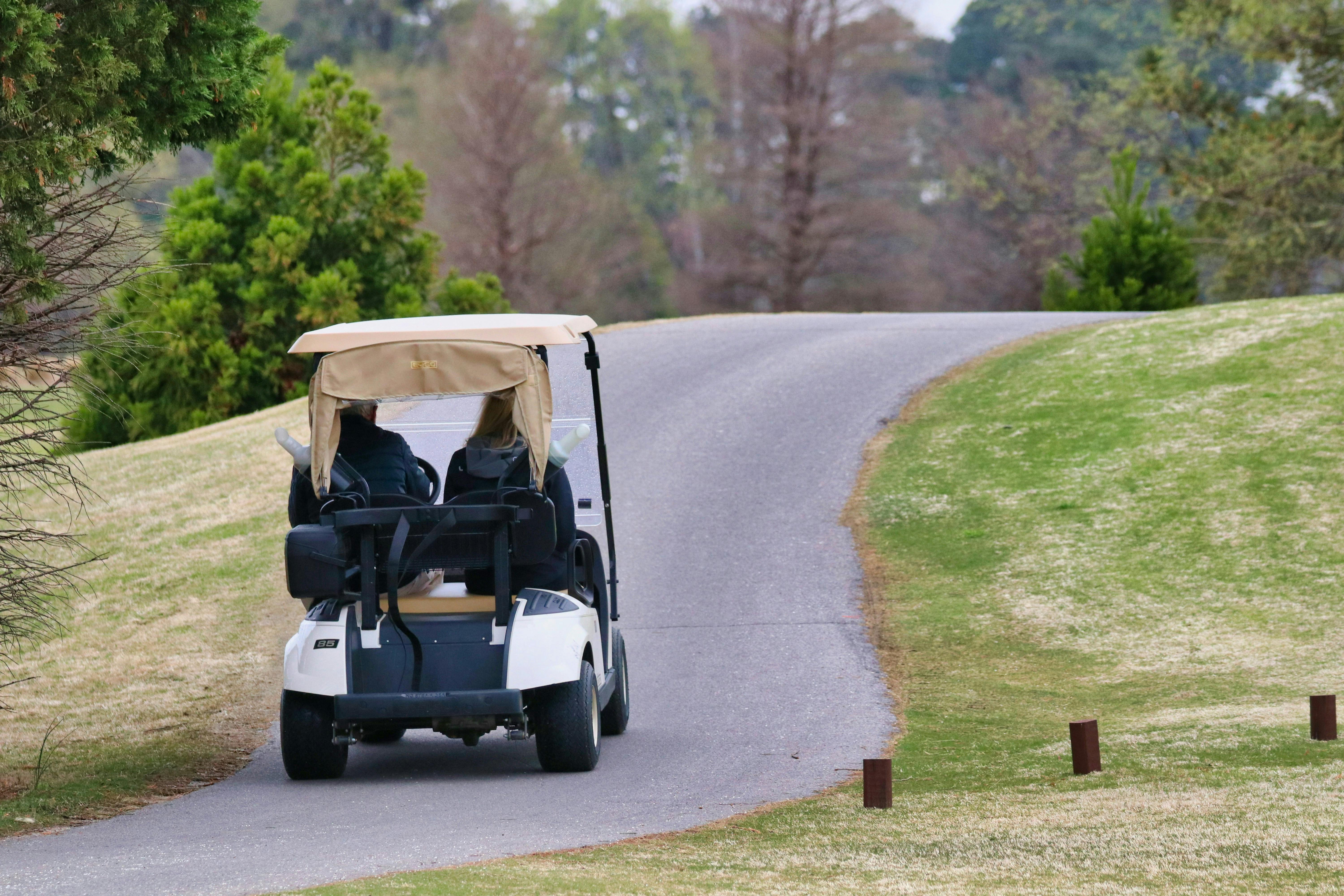 A golf cart moving away from the viewer on a golf course pathway