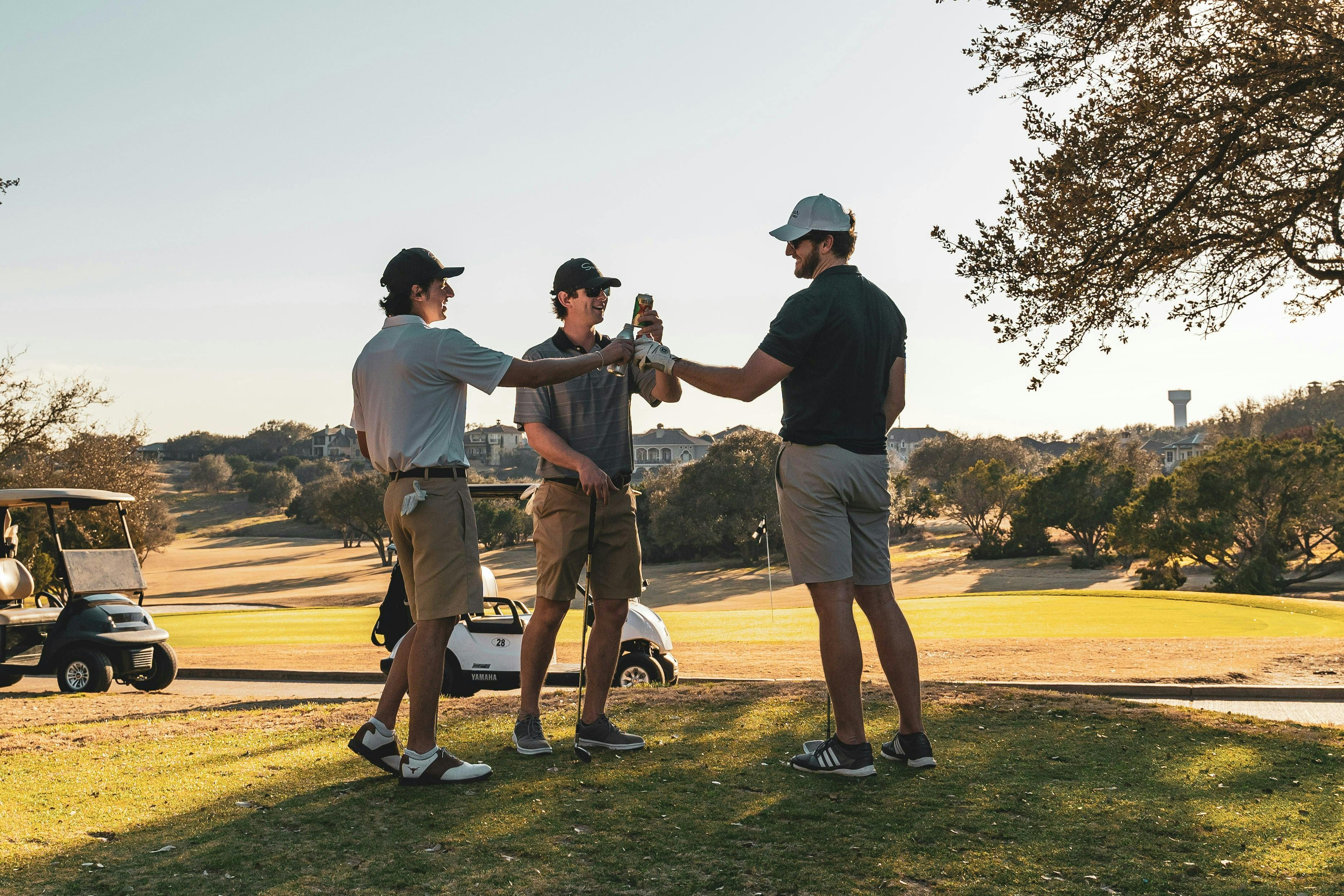 Three guys on a golf course doing a toast with beers