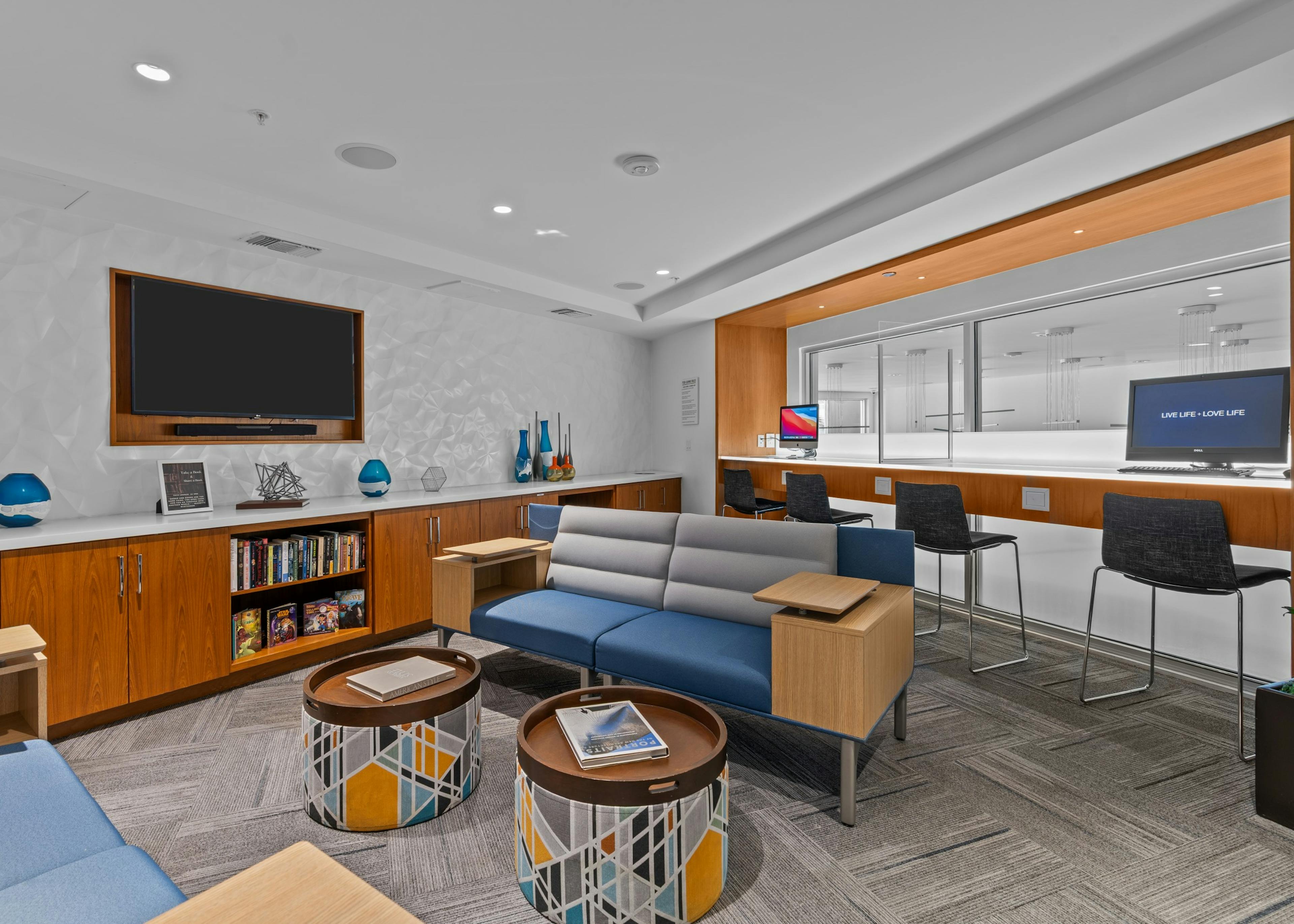 Tech lounge with two computers and various blue and gray seating and big screen TV at AMLI Uptown Orange apartments