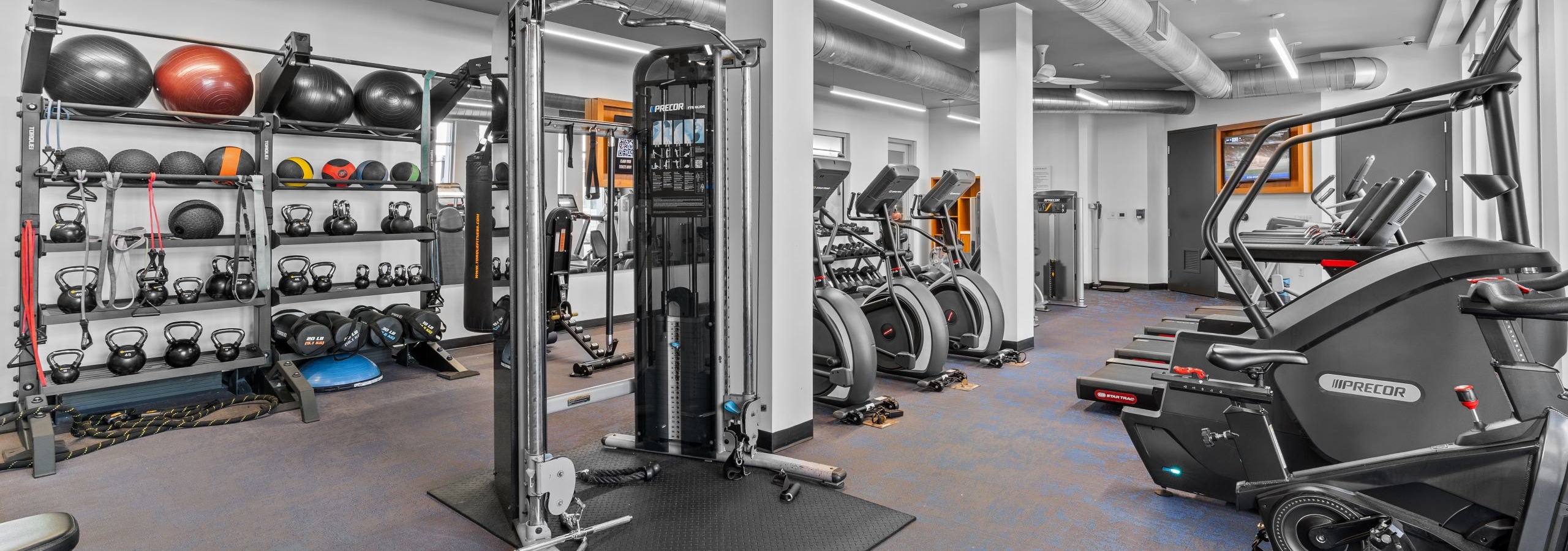 Interior of fitness center at AMLI Uptown Orange apartments with cardio machines, free weights and medicine balls