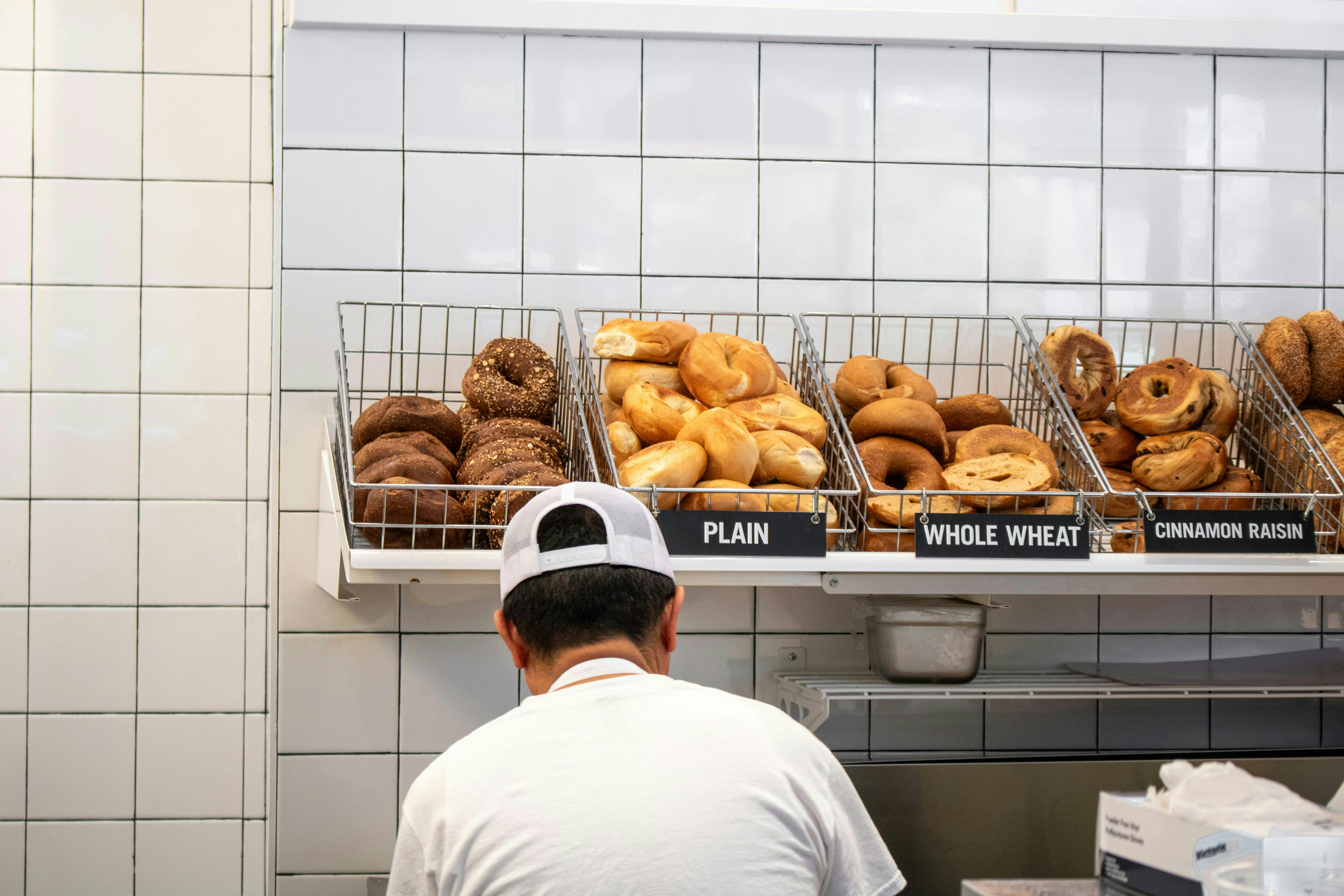 A baker in front of a display case full of bagels of all kinds