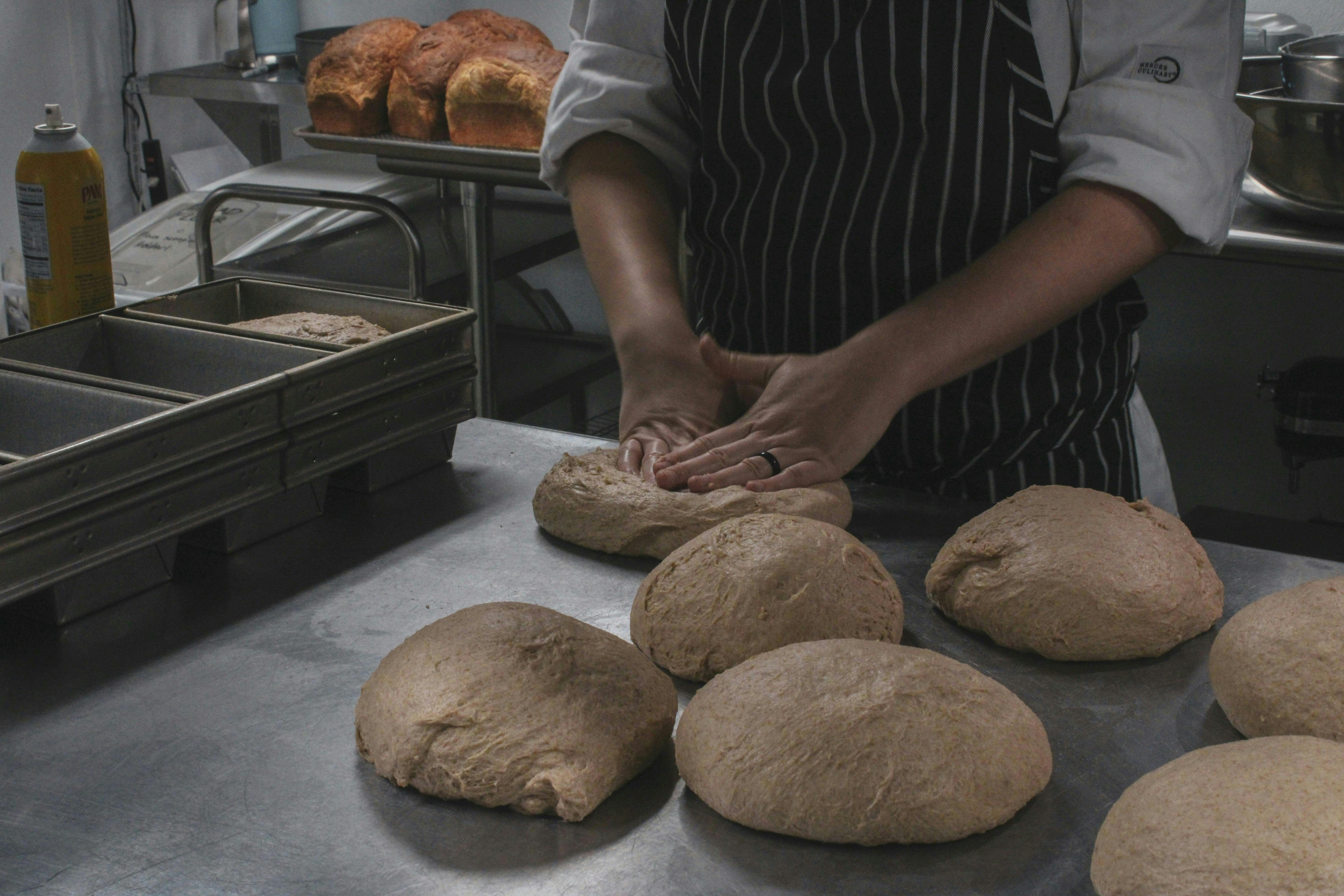 A man kneading a table full of round bread loaf dough