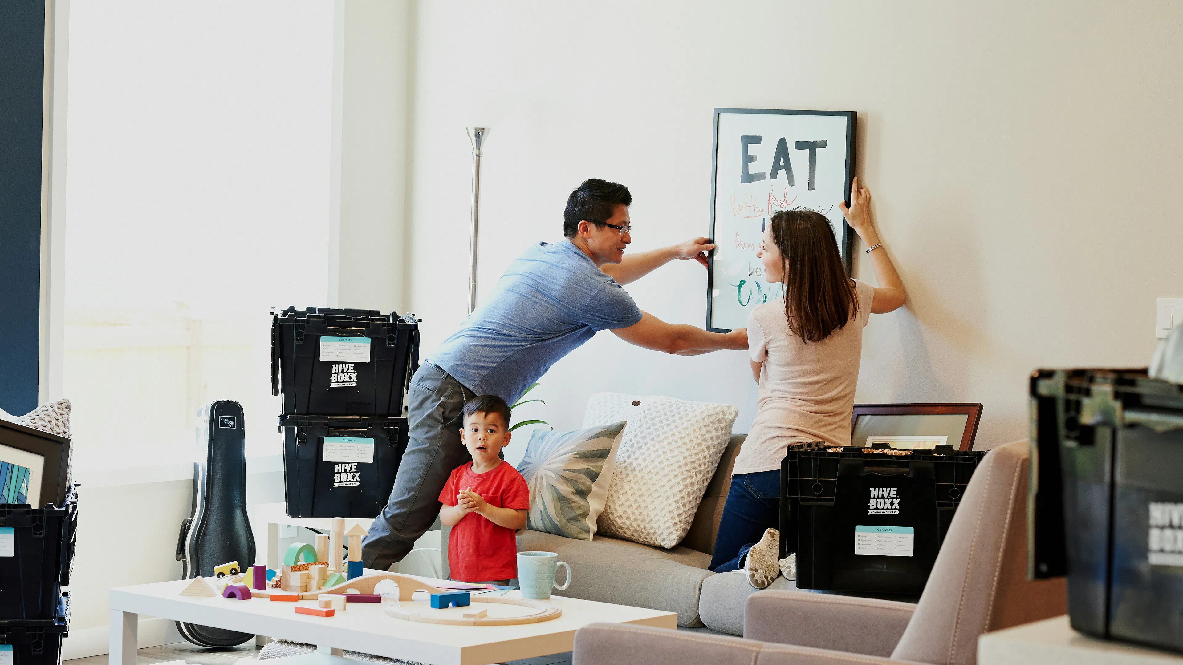A man and woman hanging a picture on a wall with a small child nearby
