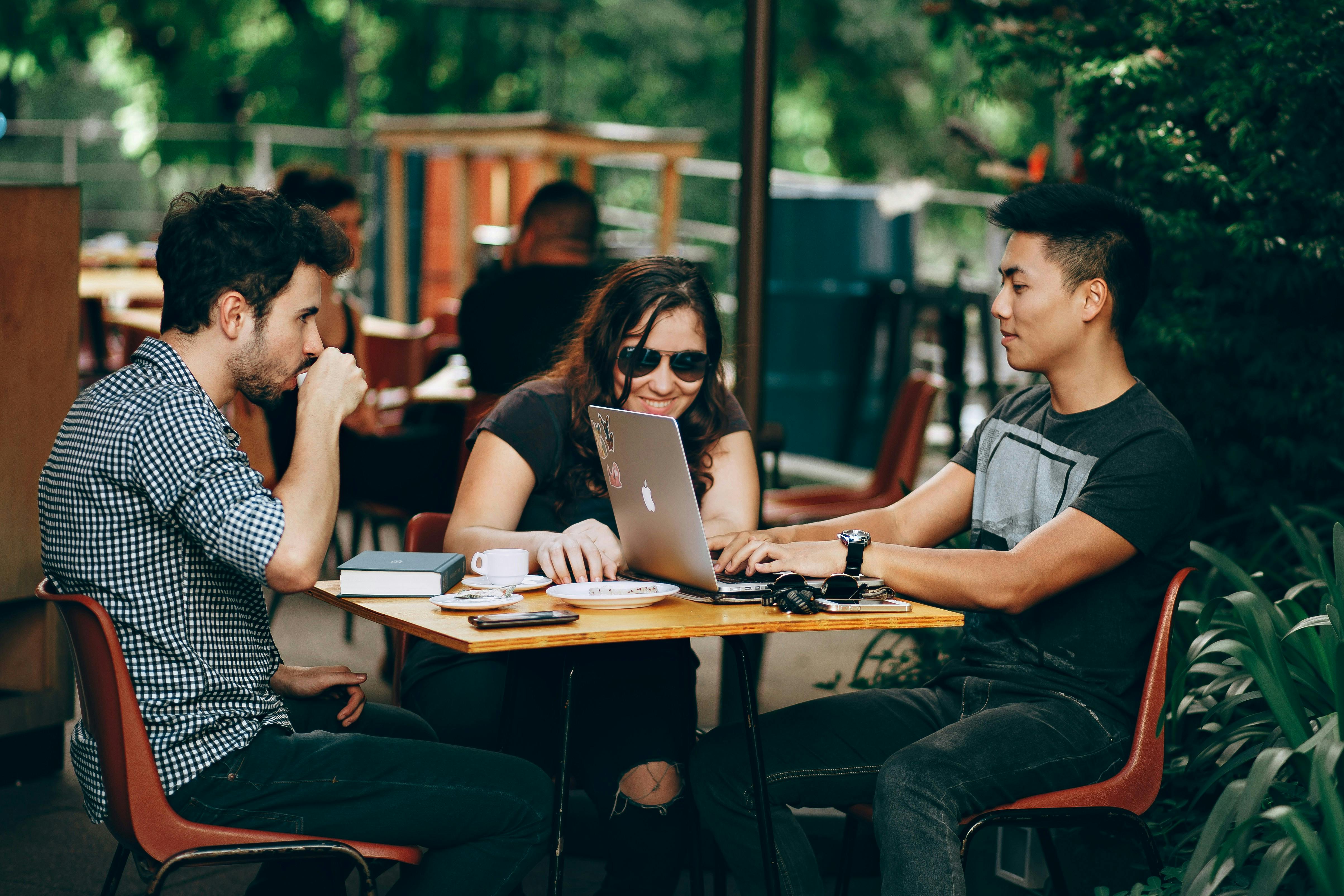 Three people outside at a small outdoor table with their laptops