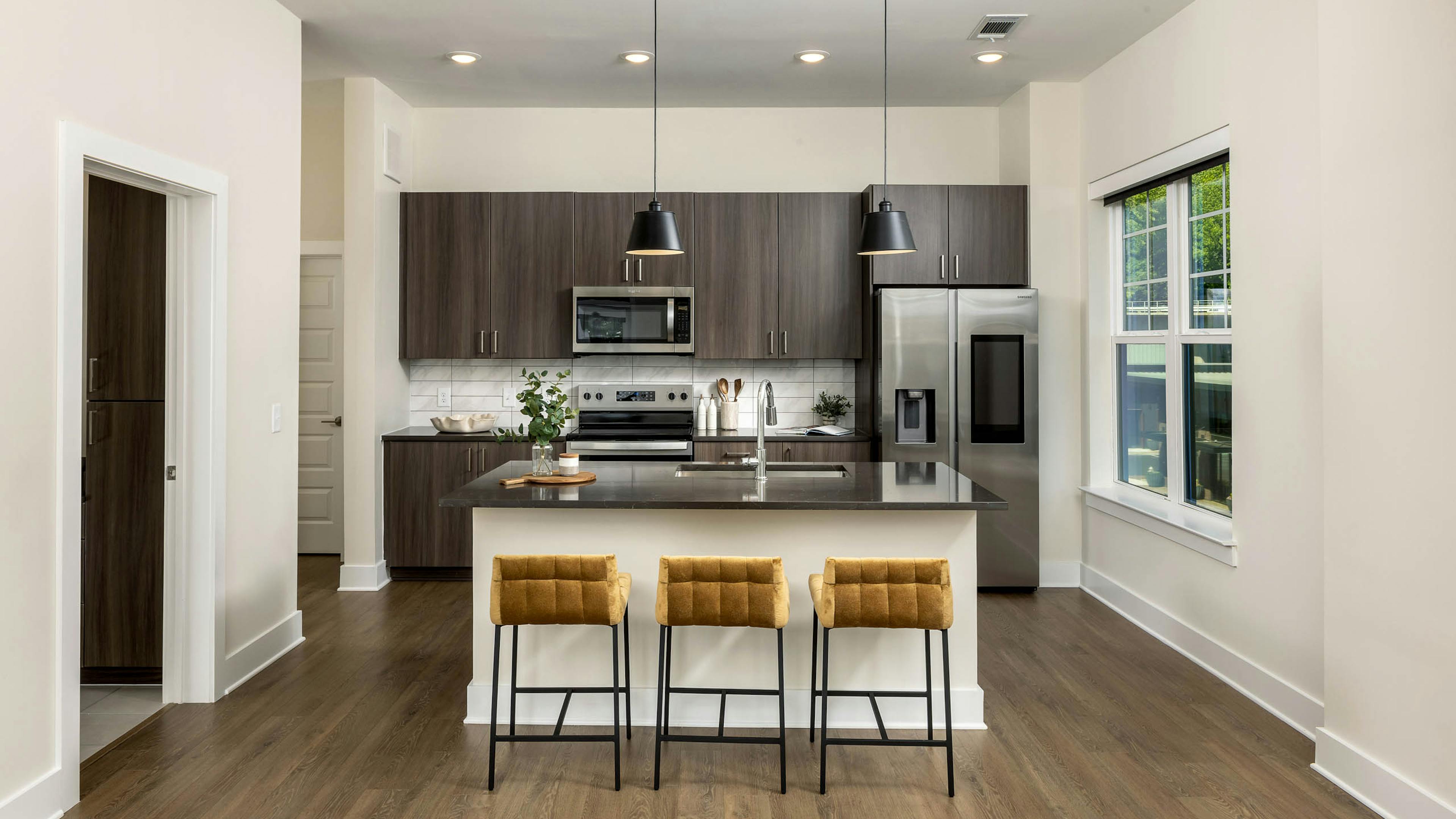 Interior view of a kitchen at AMLI Brookhaven with an island with black countertop with a basin sink with padded gold stools