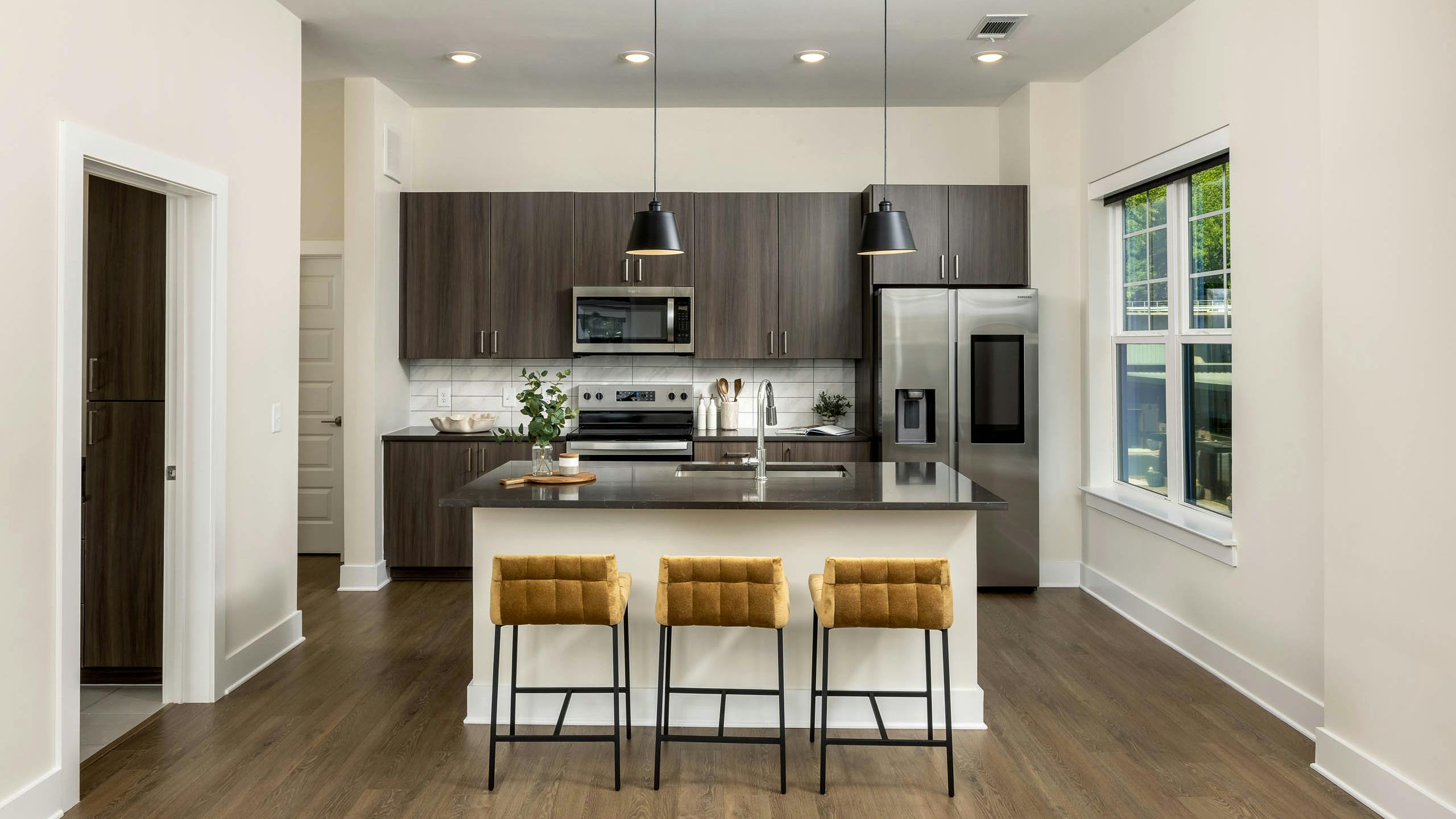 Interior view of a kitchen at AMLI Brookhaven with an island with black countertop with a basin sink with padded gold stools