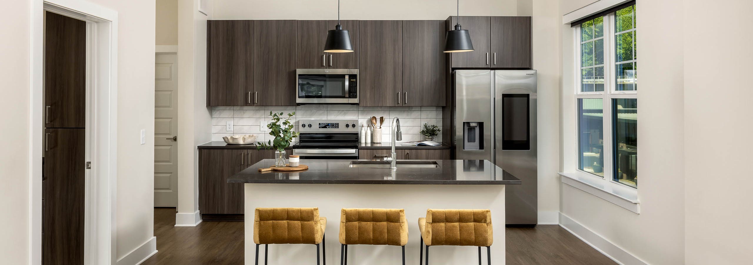 Interior view of a kitchen at AMLI Brookhaven with an island with black countertop with a basin sink with padded gold stools