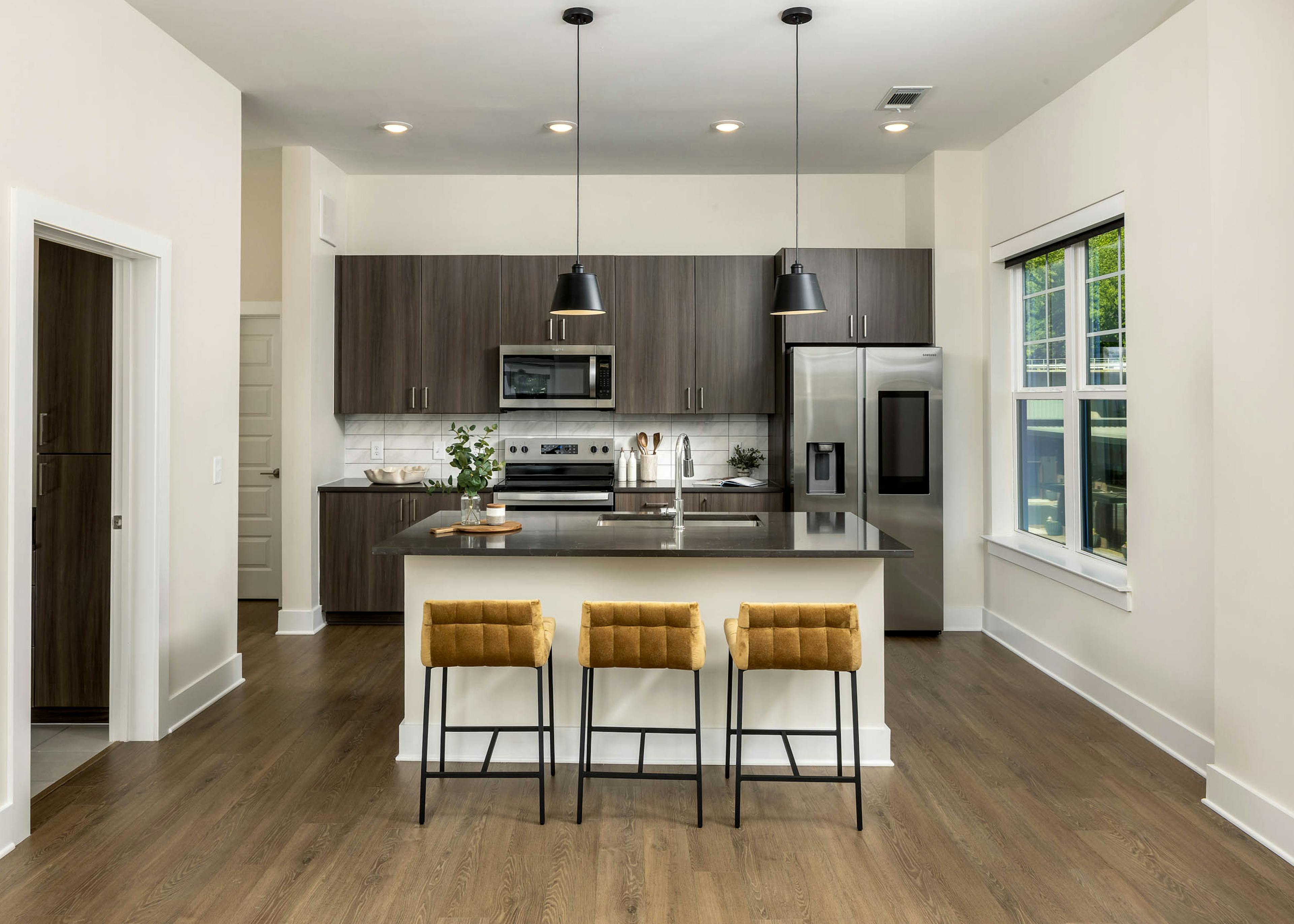 Interior view of a kitchen at AMLI Brookhaven with an island with black countertop with a basin sink with padded gold stools