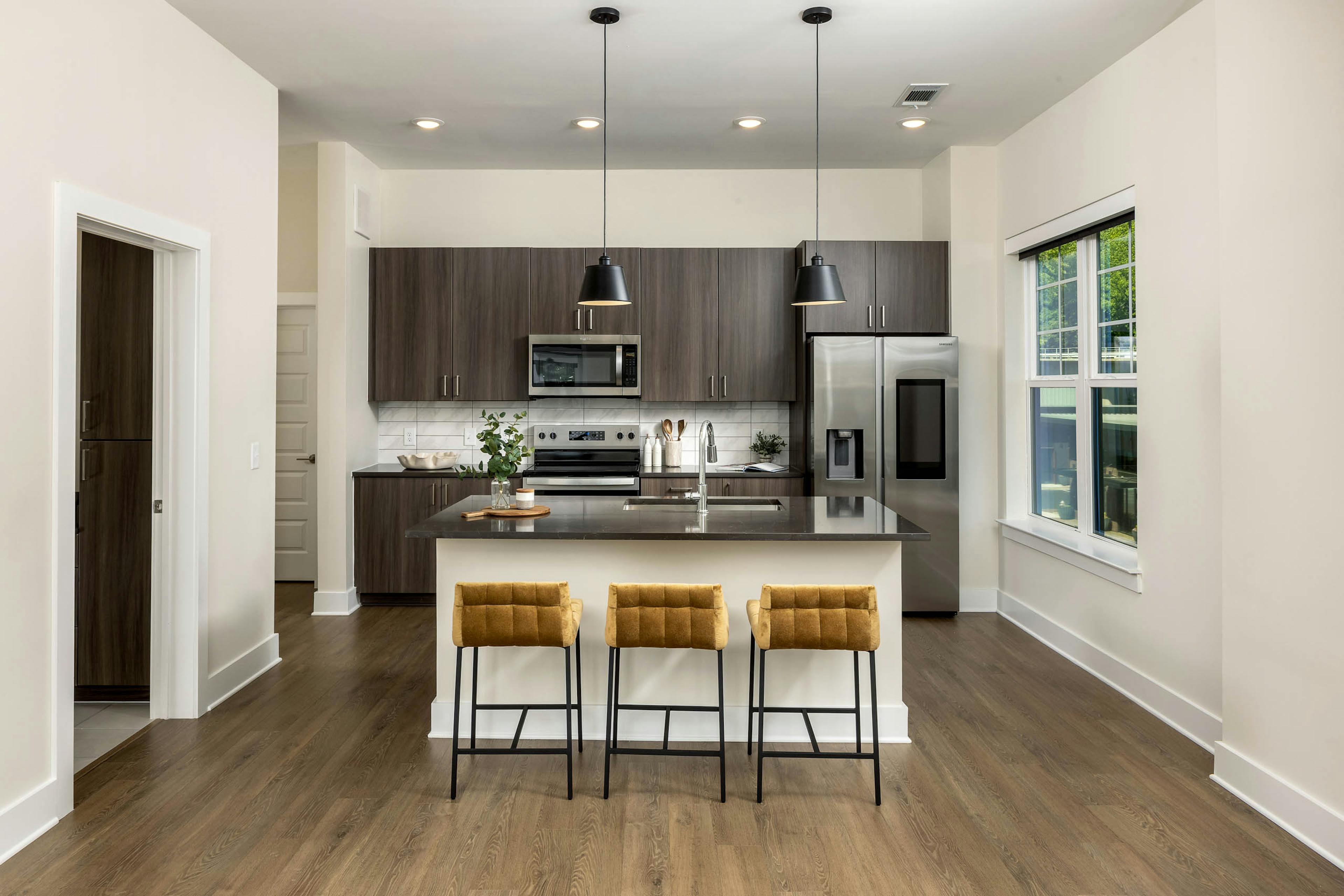 Interior view of a kitchen at AMLI Brookhaven with an island with black countertop with a basin sink with padded gold stools