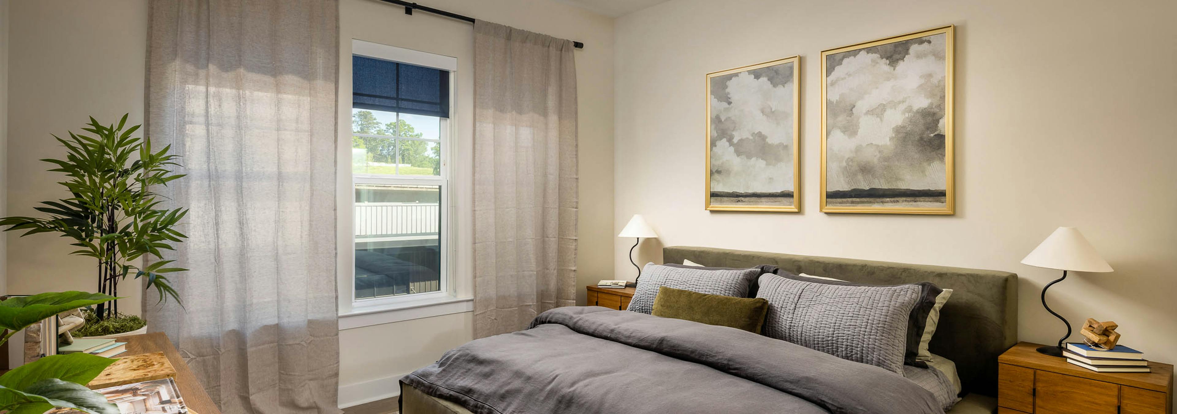 Bedroom at AMLI Brookhaven apartments with hardwood flooring and a ceiling fan and a bed with a grey comforter blanket and a window