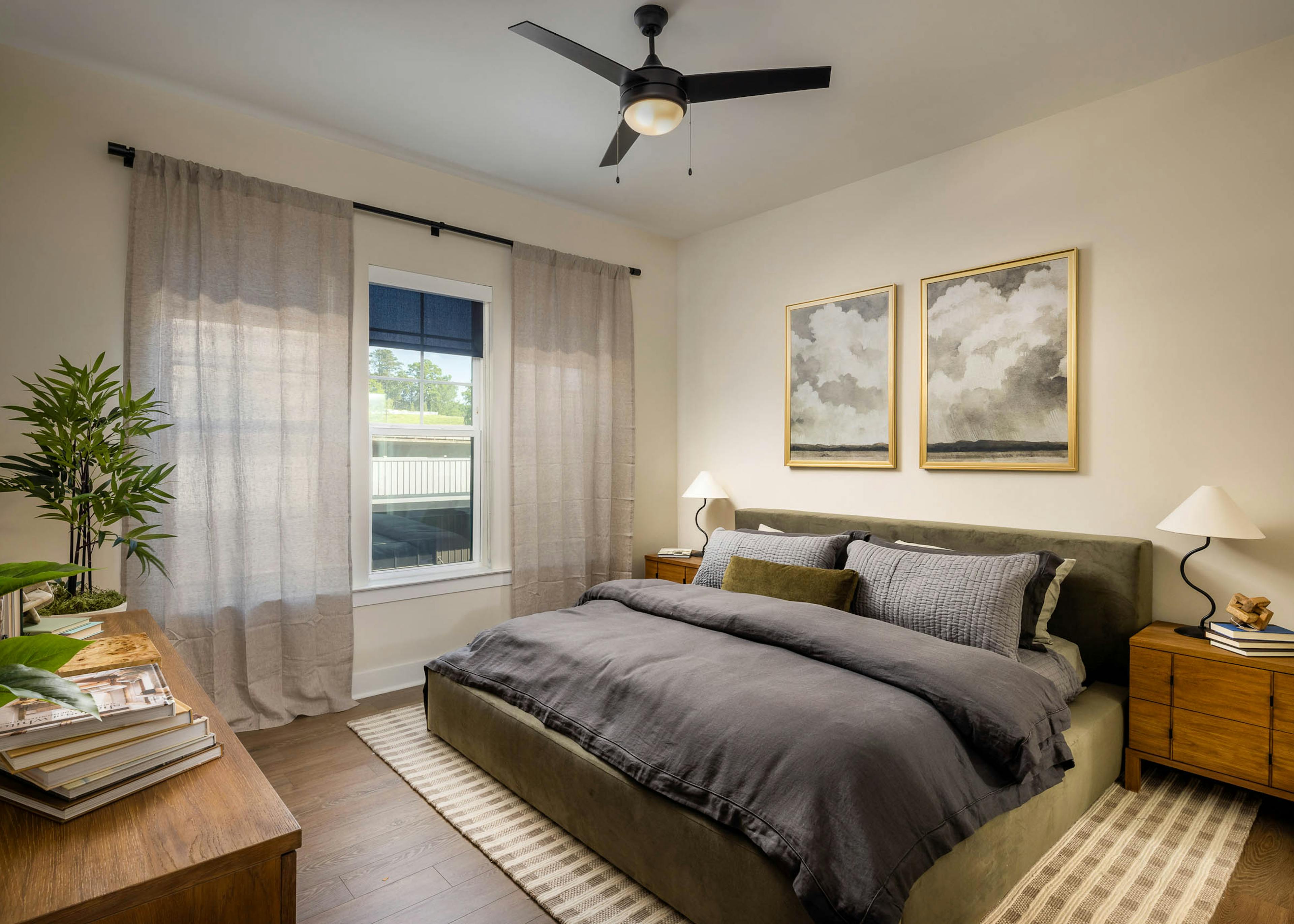 Bedroom at AMLI Brookhaven apartments with hardwood flooring and a ceiling fan and a bed with a grey comforter blanket and a window