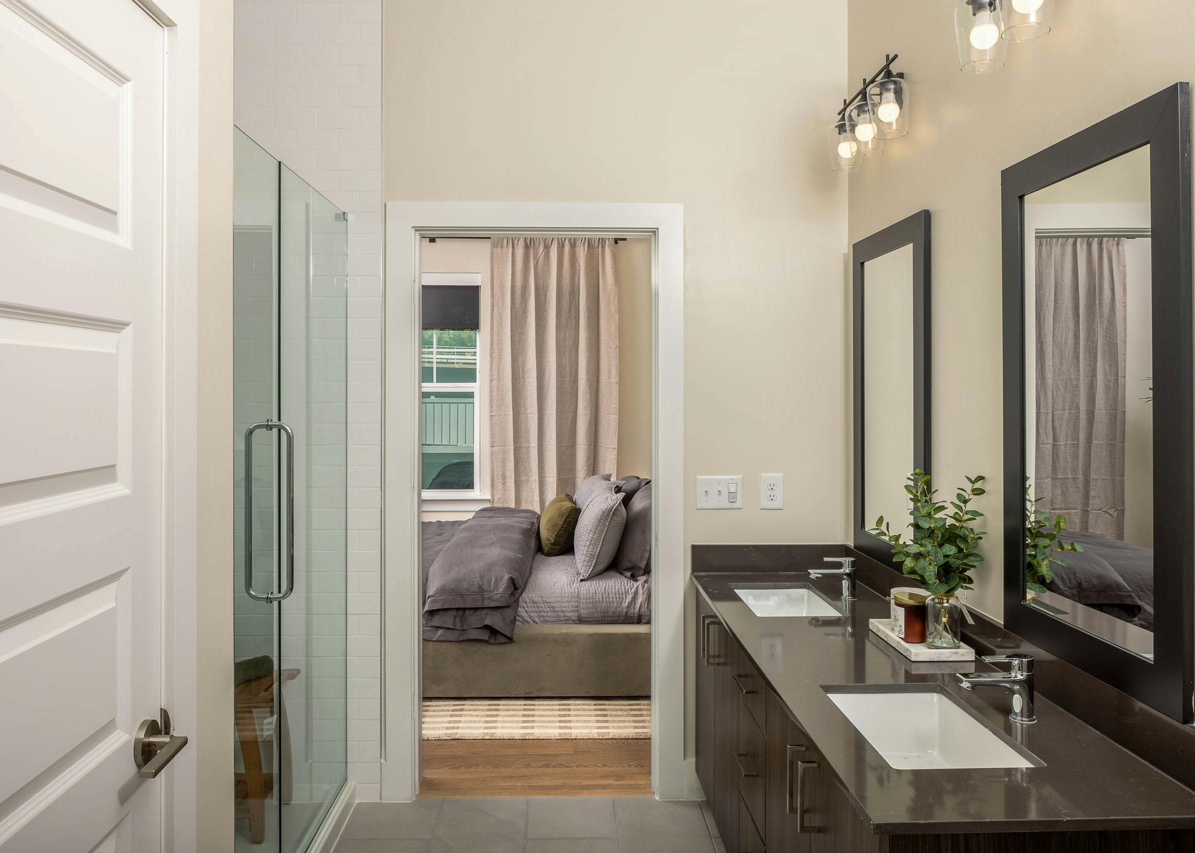 AMLI Brookhaven bathroom with two sinks and mirrors with black borders and a glass door shower with a view into the bedroom