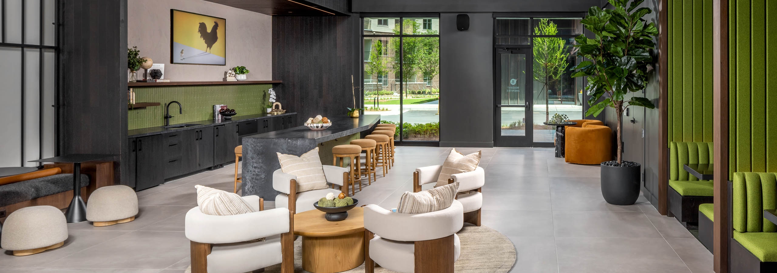A coworking space kitchen area at AMLI Brookhaven with a long bar top with padded stools and green booths and other seating