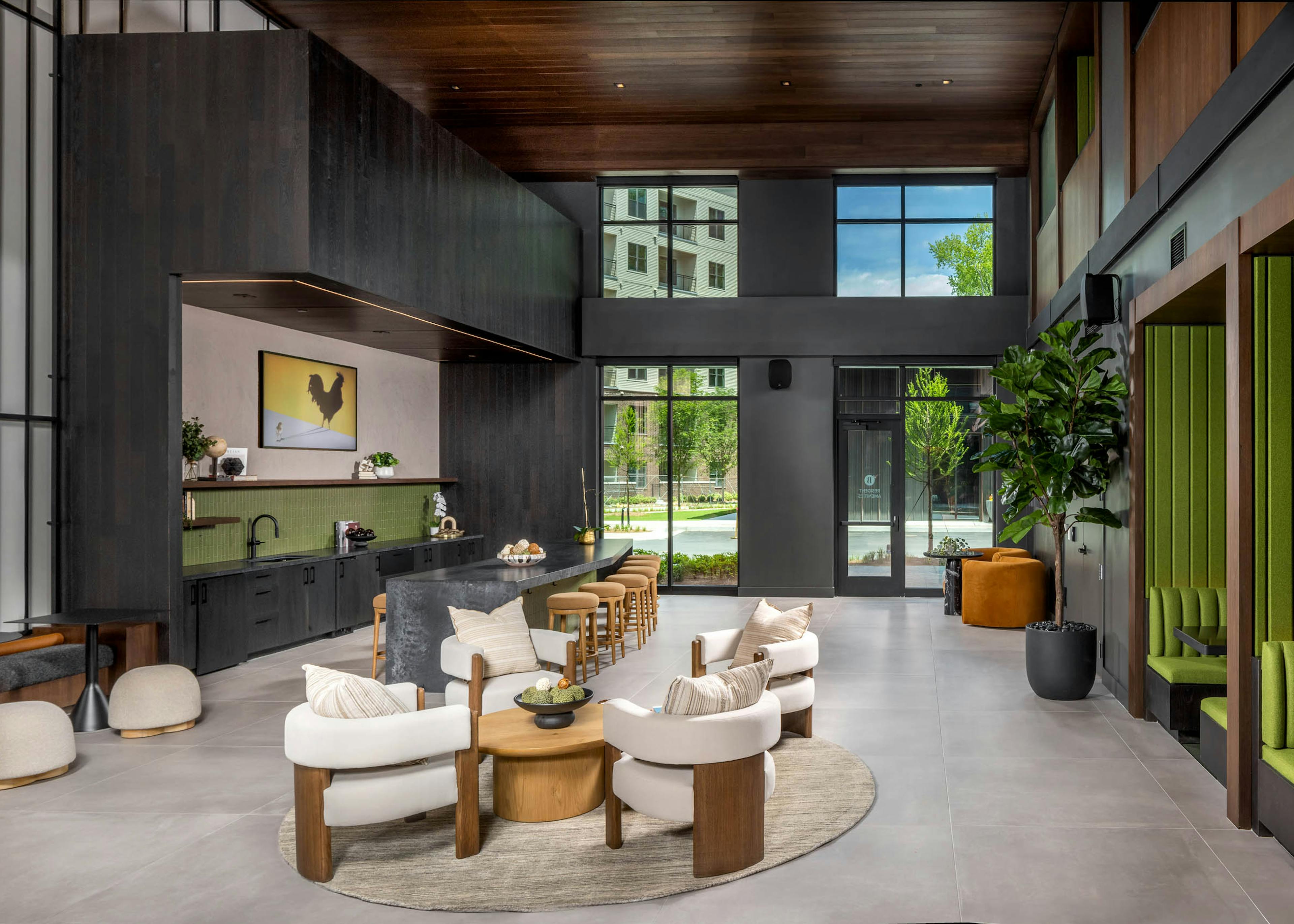 A coworking space kitchen area at AMLI Brookhaven with a long bar top with padded stools and green booths and other seating