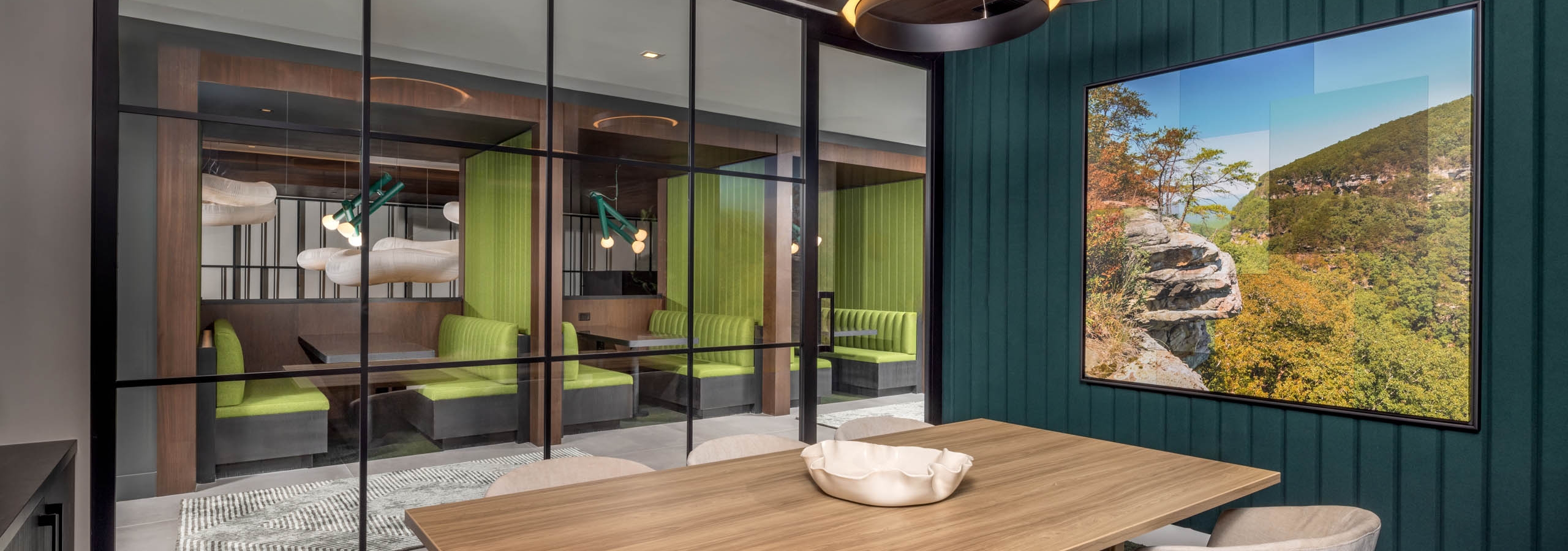A conference room at AMLI Brookhaven apartments with a wood table and chairs and a large piece of wall art and a glass wall